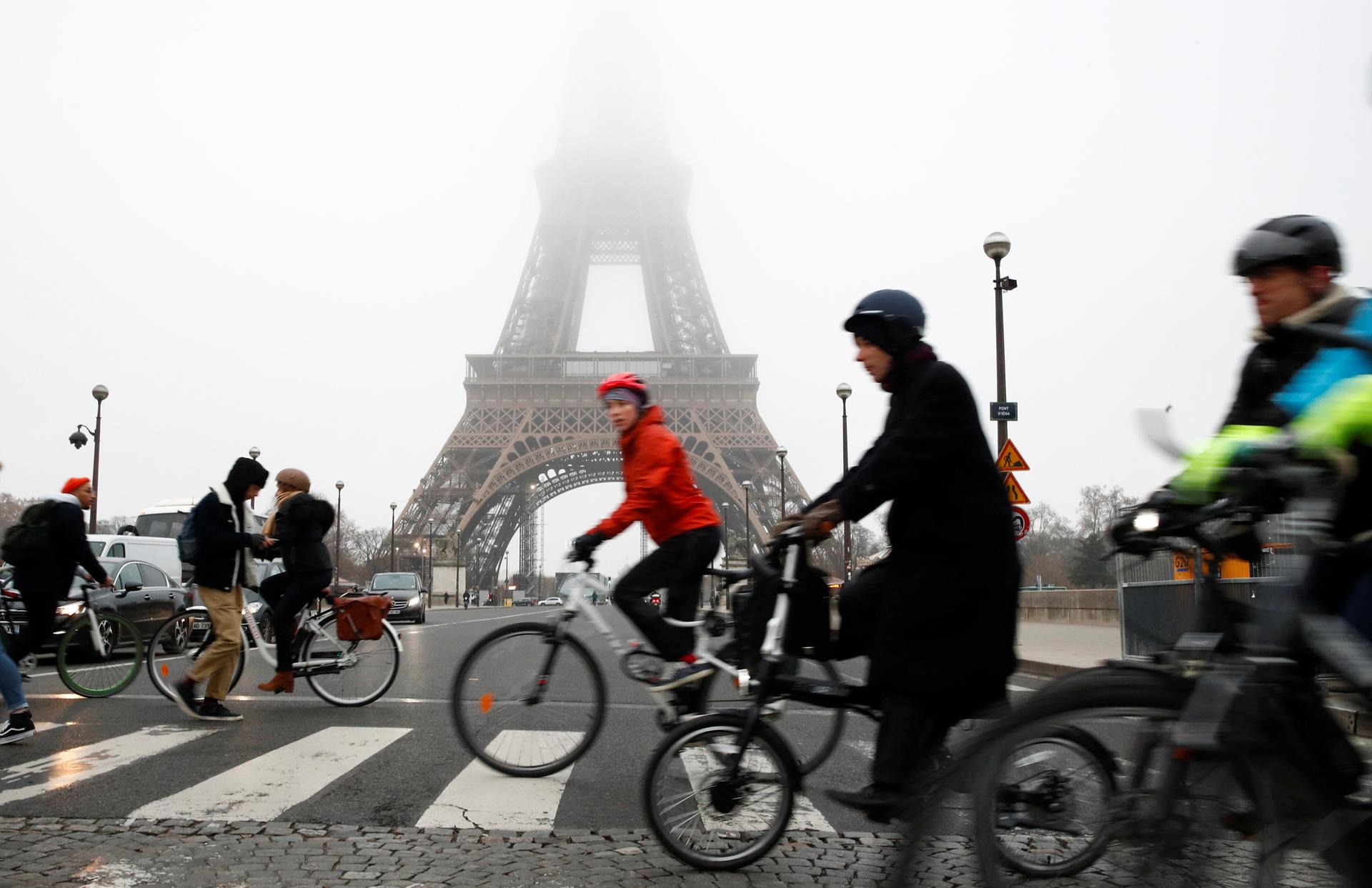 Several people are shown riding bicycles and crossing the street near the Eiffel Tower during a strike by all unions of the Paris transport network.