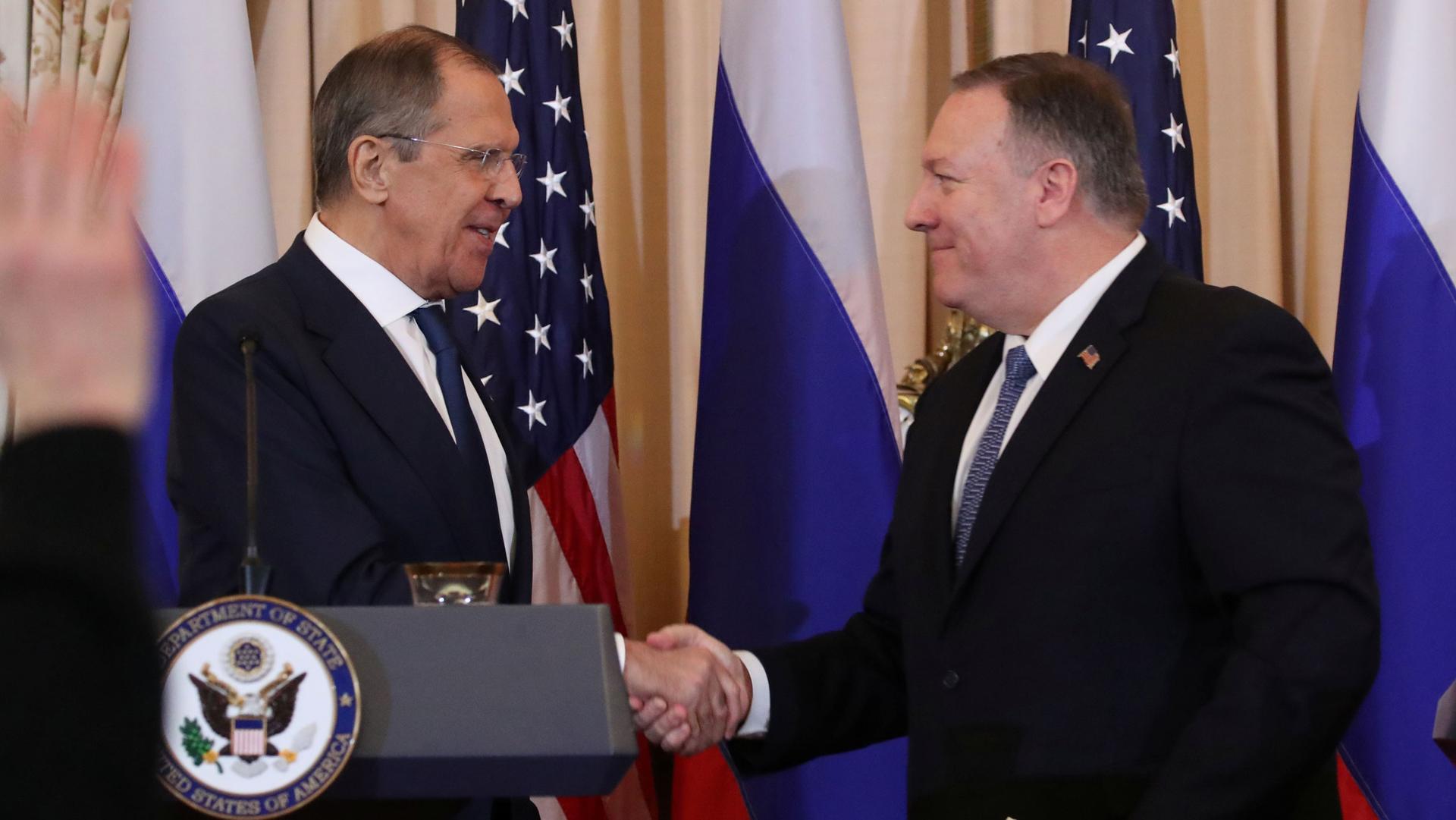 Two white men in suits shake hands, the US State Department podium is visible.