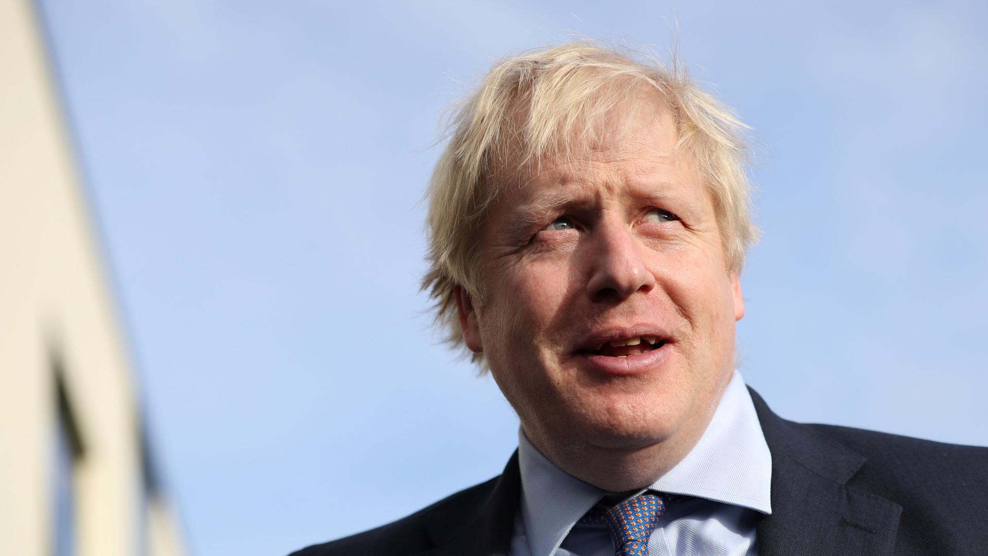British Prime Minister Boris Johnson is shown in a close-up photo wearing a red and blue tie with a blue sky in the background.