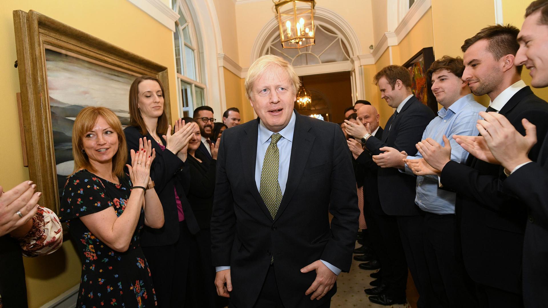 Britain's Prime Minister Boris Johnson is shown walking down a hallway with staff applauding on either side.