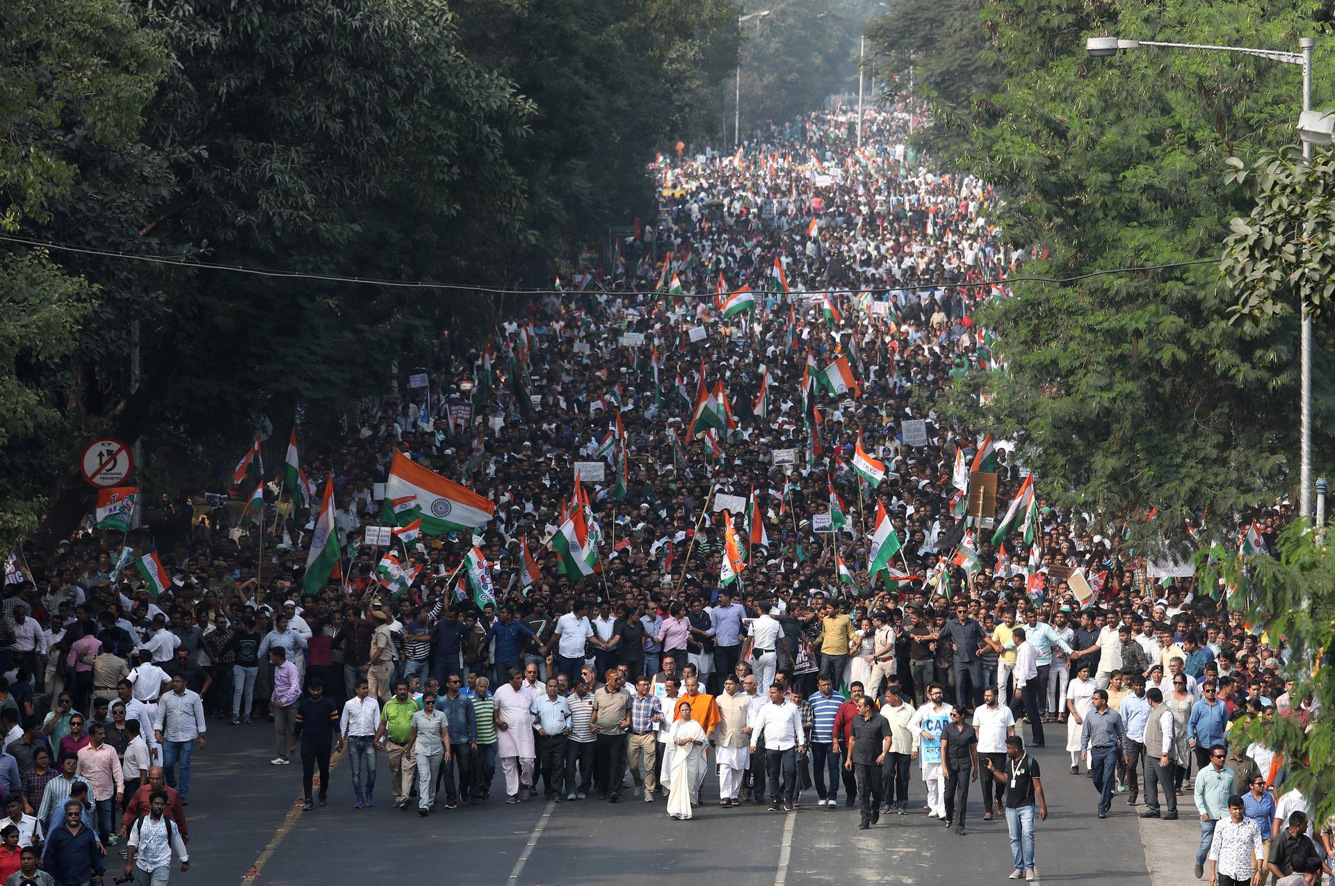 A street is filled with hundreds of protesters, many carrying India's national flag.
