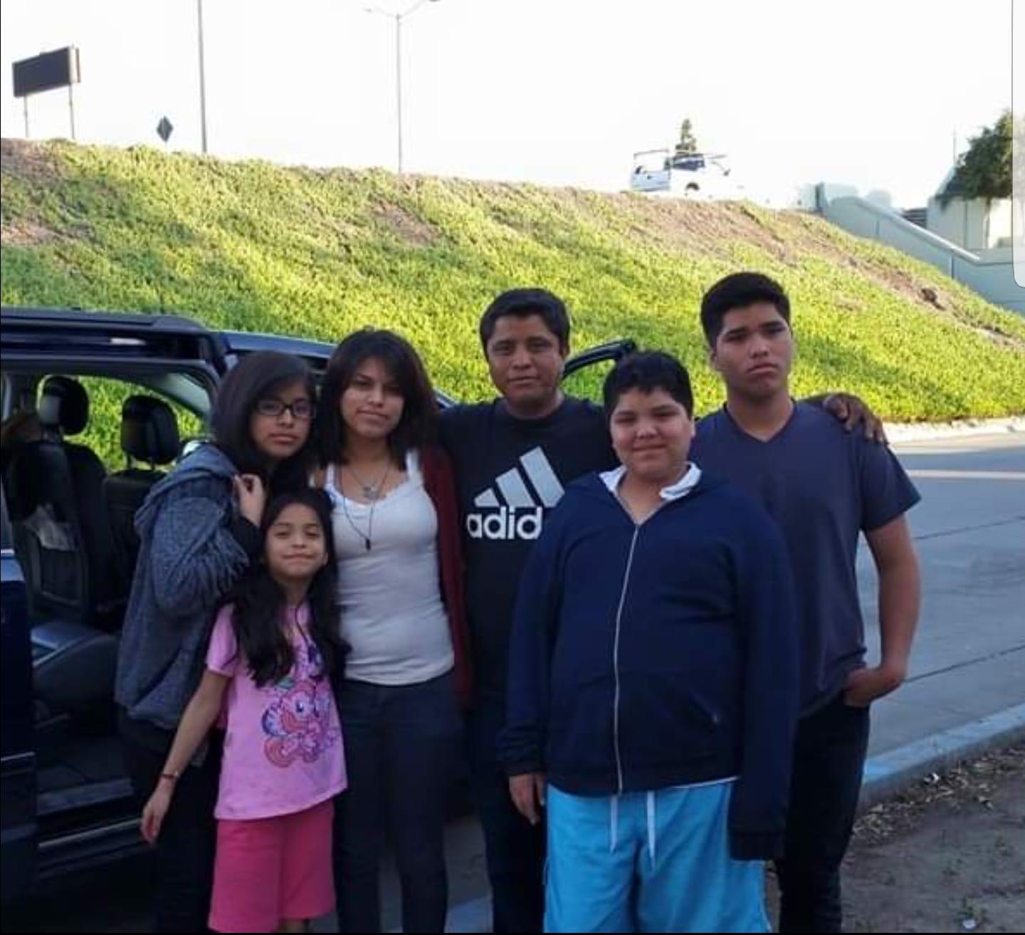 A family stands in front of car near a green hill