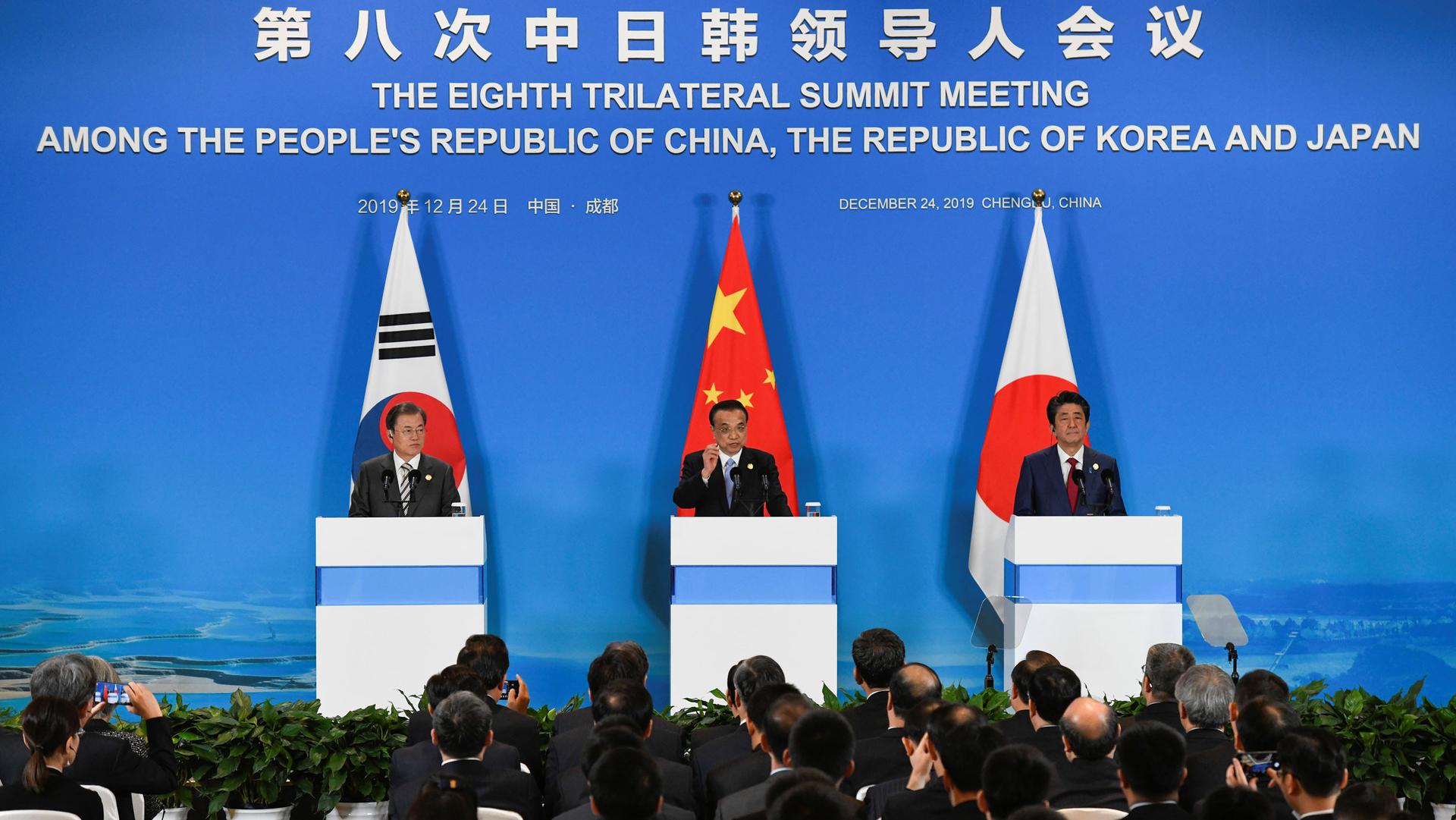 China's Premier Li Keqiang, Japan's Prime Minister Shinzo Abe and South Korea's President Moon Jae-in are shown standing behind three podiums with national flags.