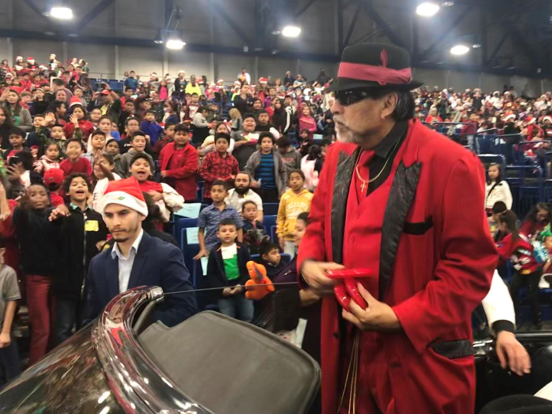 Pancho Claus is shown in a red jacket and black hat standing in a car with a large crowd behind him.