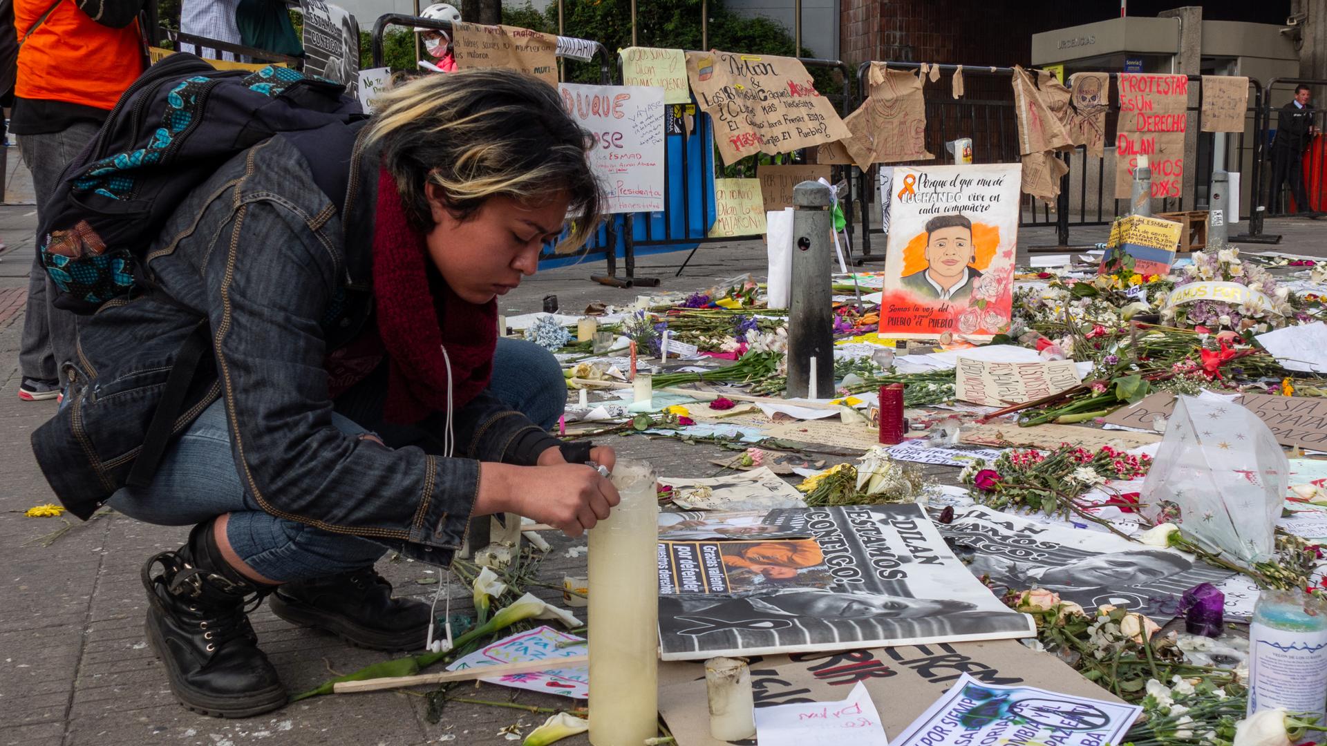 A student leans over a candle at a memorial with lots of photos and paintings 