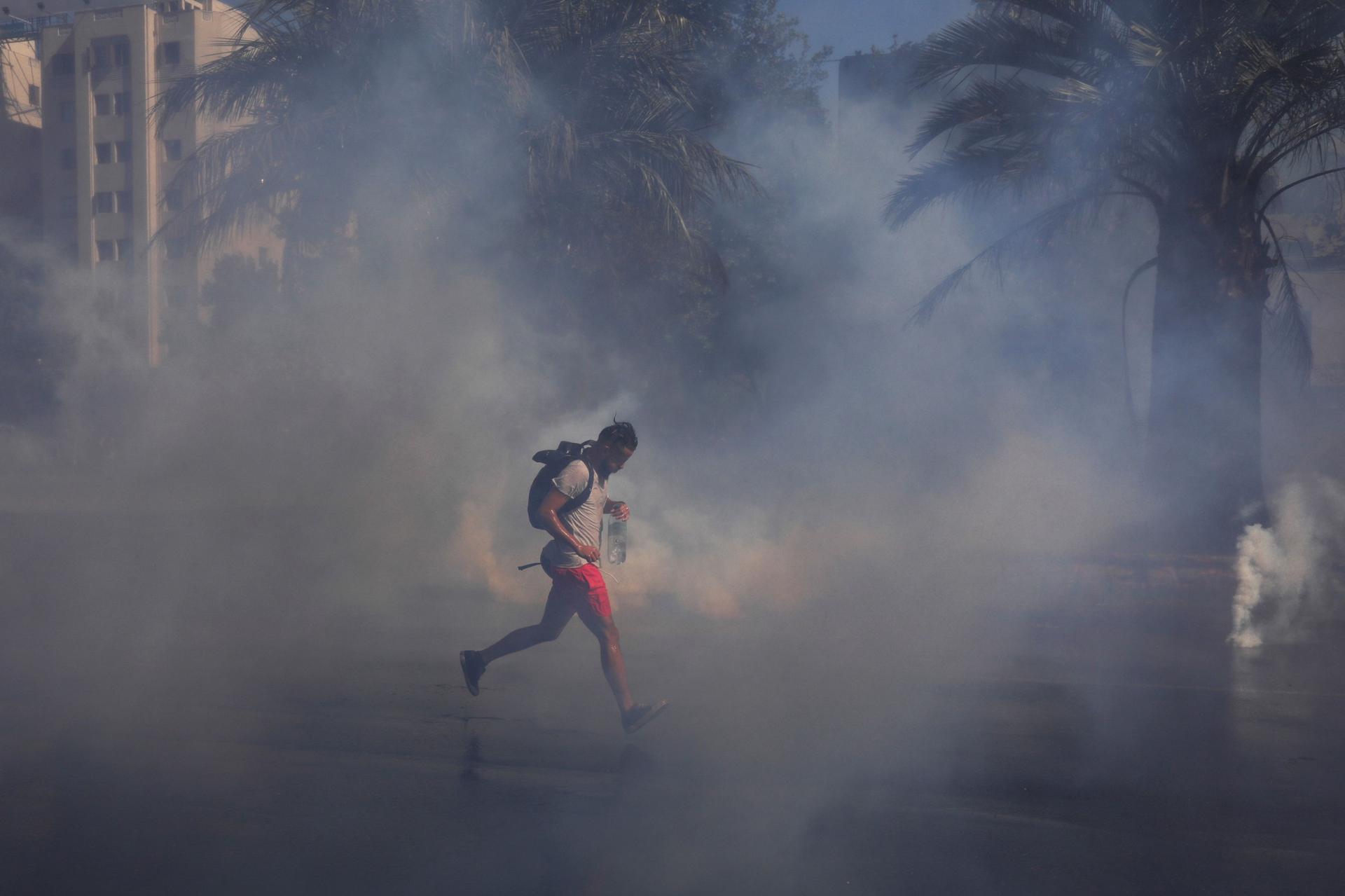 A demonstrator wearing red shorts and carrying a backpack, runs amid tear gas.