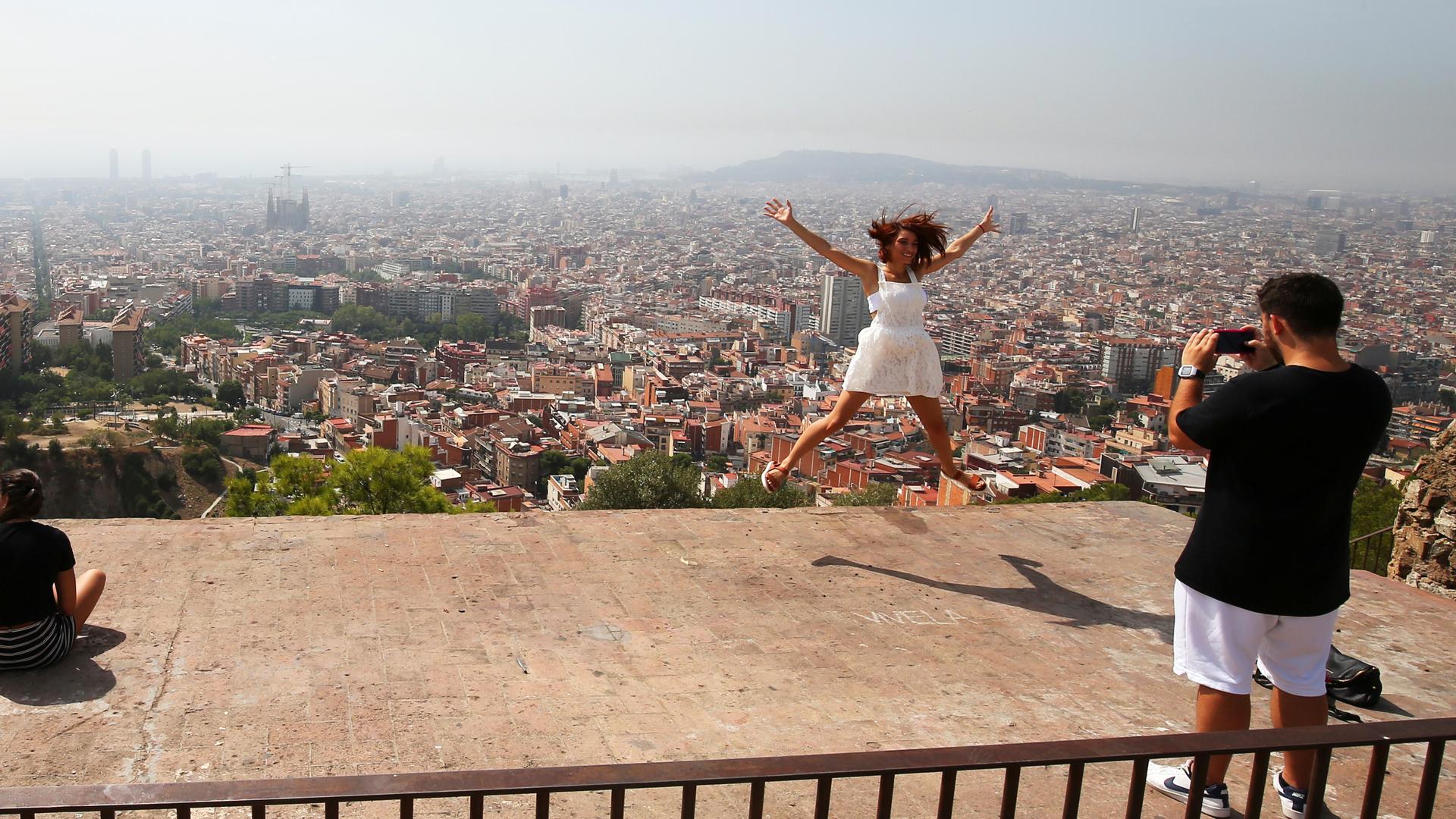 A tourist leaps in the air with a backdrop of the skyline of Barcelona 