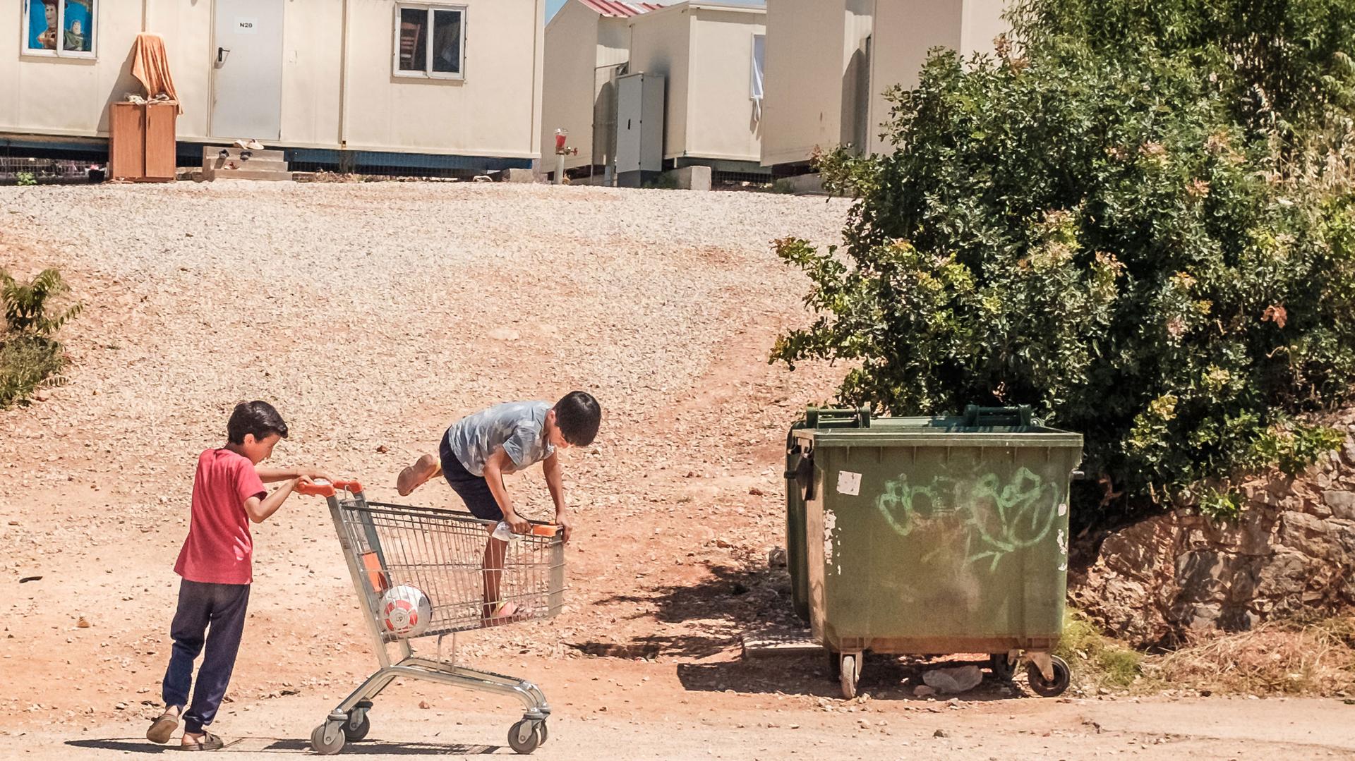 Two young children are shown playing with a grocery cart with container homes shown in the background.