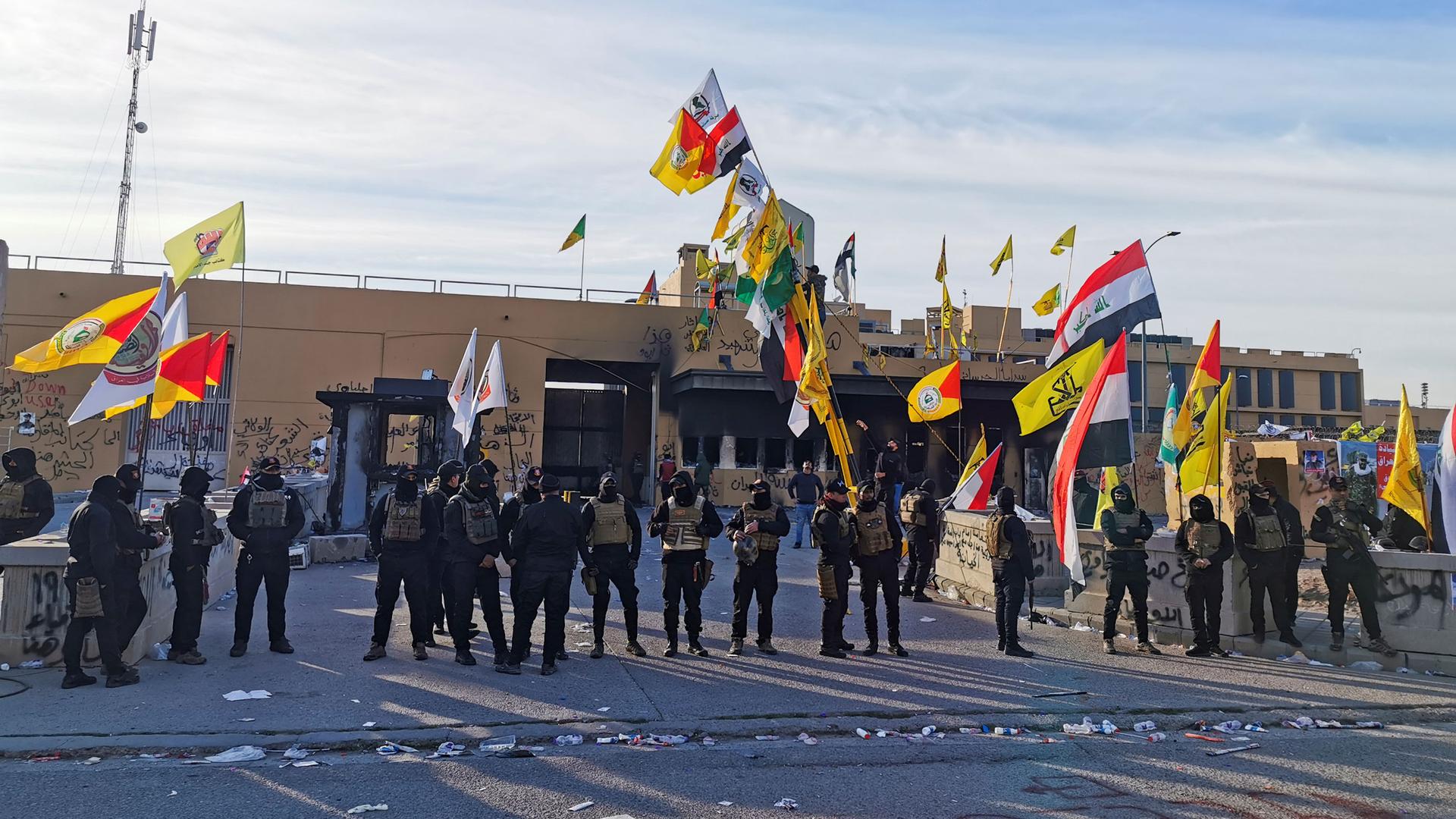 A line of security forces wearing helmets and carrying weapons are shown standing outside of the US Embassy in Baghdad.