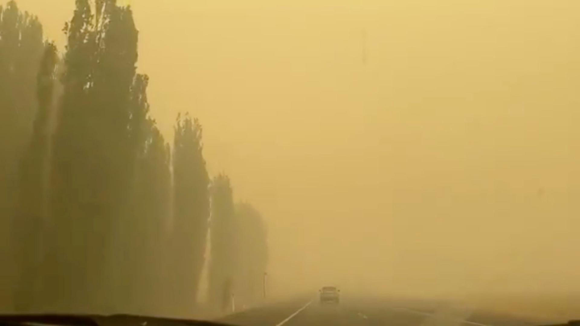 A car is shown in the distance driving on a road and entirely surrounded by dark yellow smoke.