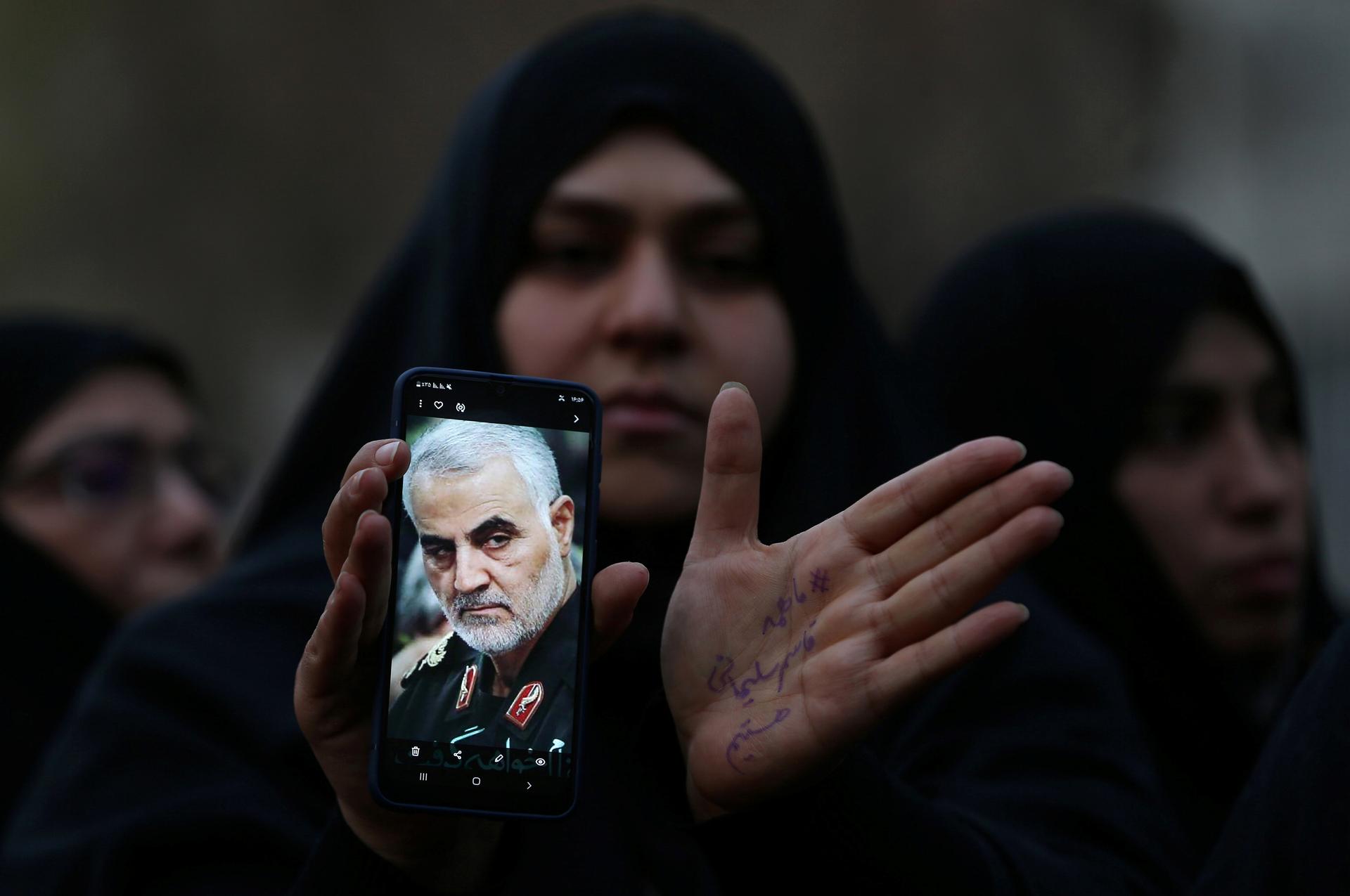 A woman wearing an abaya holds a cellphone with the photo of an Iranian military commander.