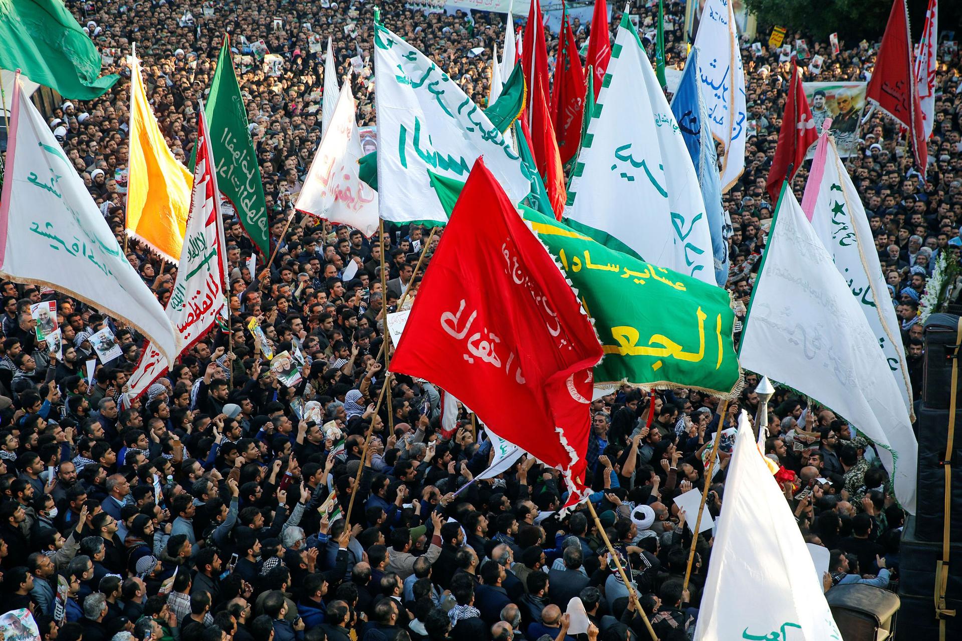 A large crowd of people are shown from above with dozens of flags waving.