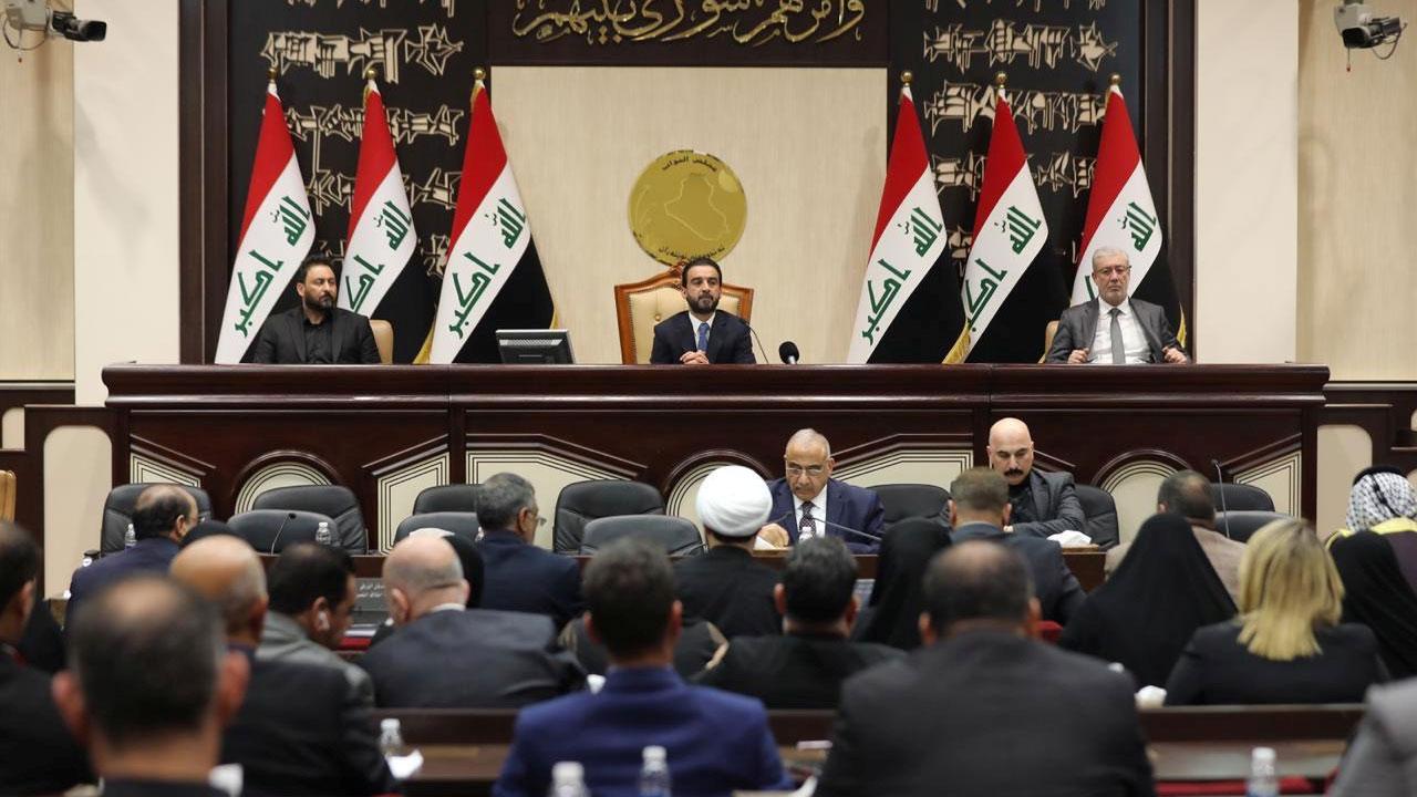 Three leaders of Iraq's paliament are shown sitting at the front of a large room with other lawmakers.
