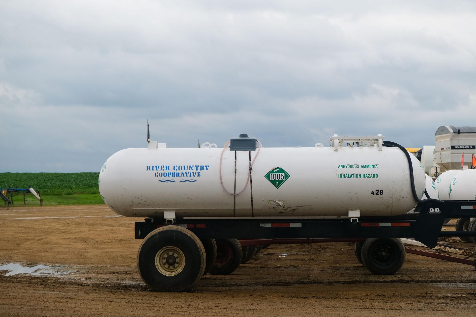A trailer with a tank of anhydrous ammonia is shown parked on a dirt parking lot.