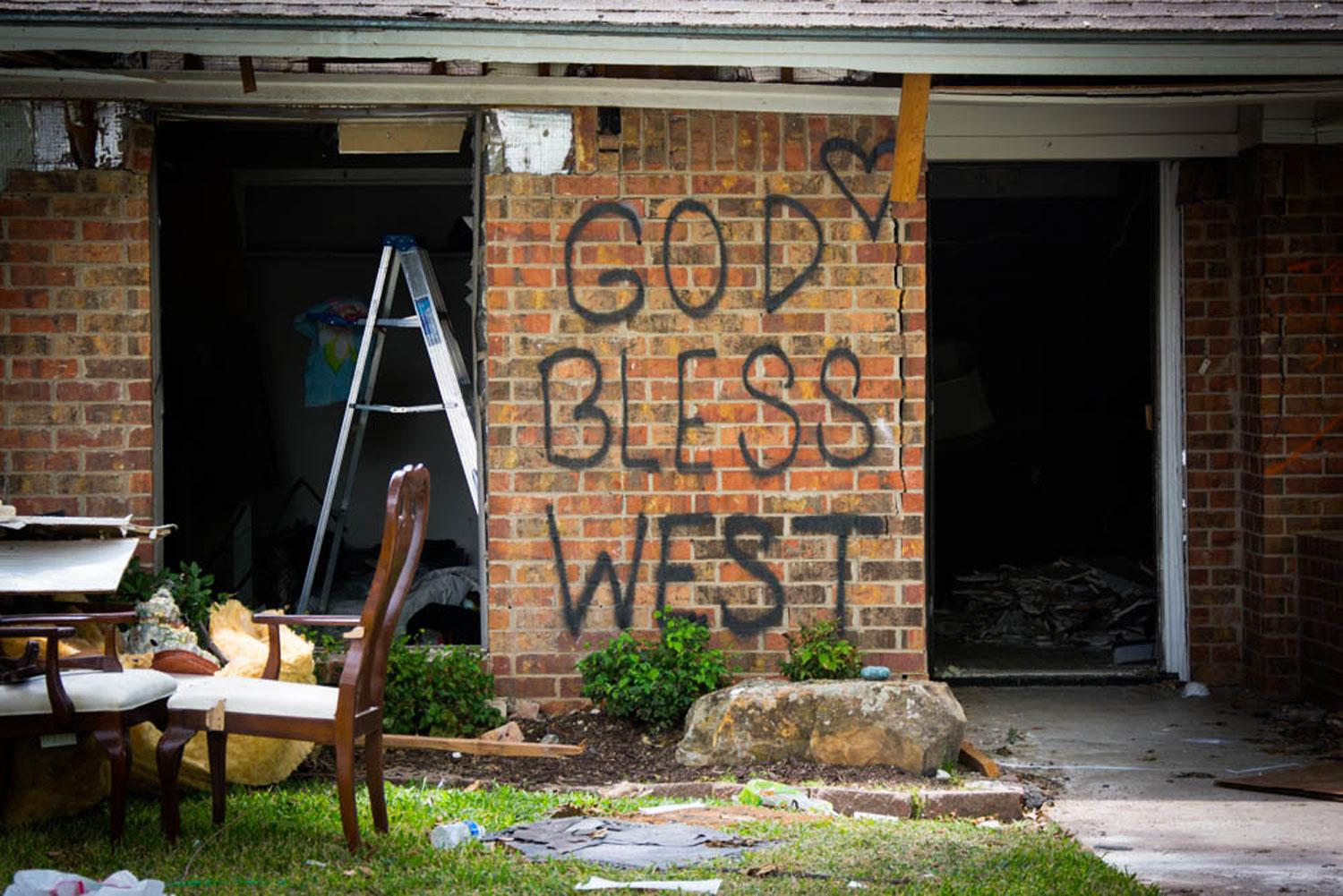 A heavily damaged home is shown with the words, 'God Bless West' spray-painted on it.
