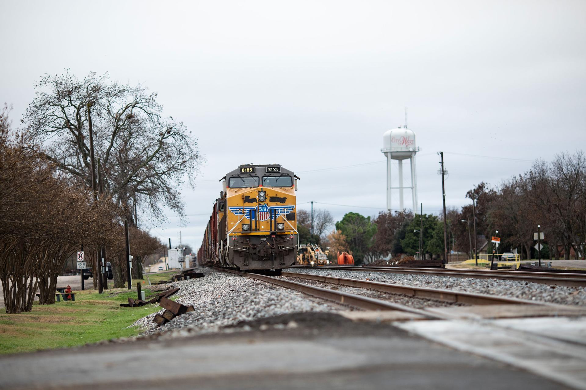 A yellow freight train is shown with a water tower in the background.
