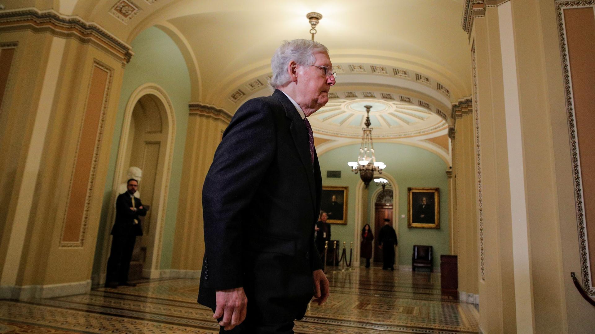 Senate Majority Leader Mitch McConnell is shown walking in the hallways of the Capitol building and wearing a dark suit.