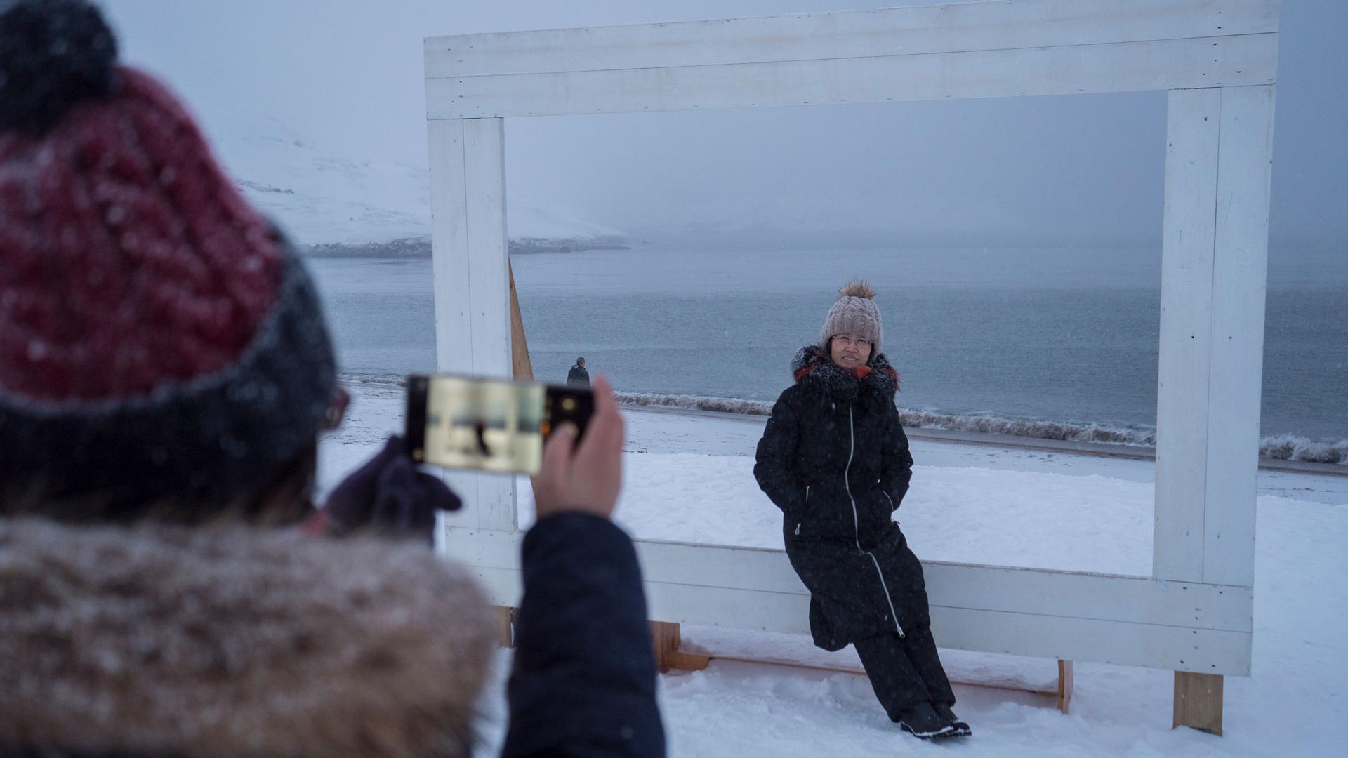 A woman is shown sitting a large frame with the Barents Sea in the background.
