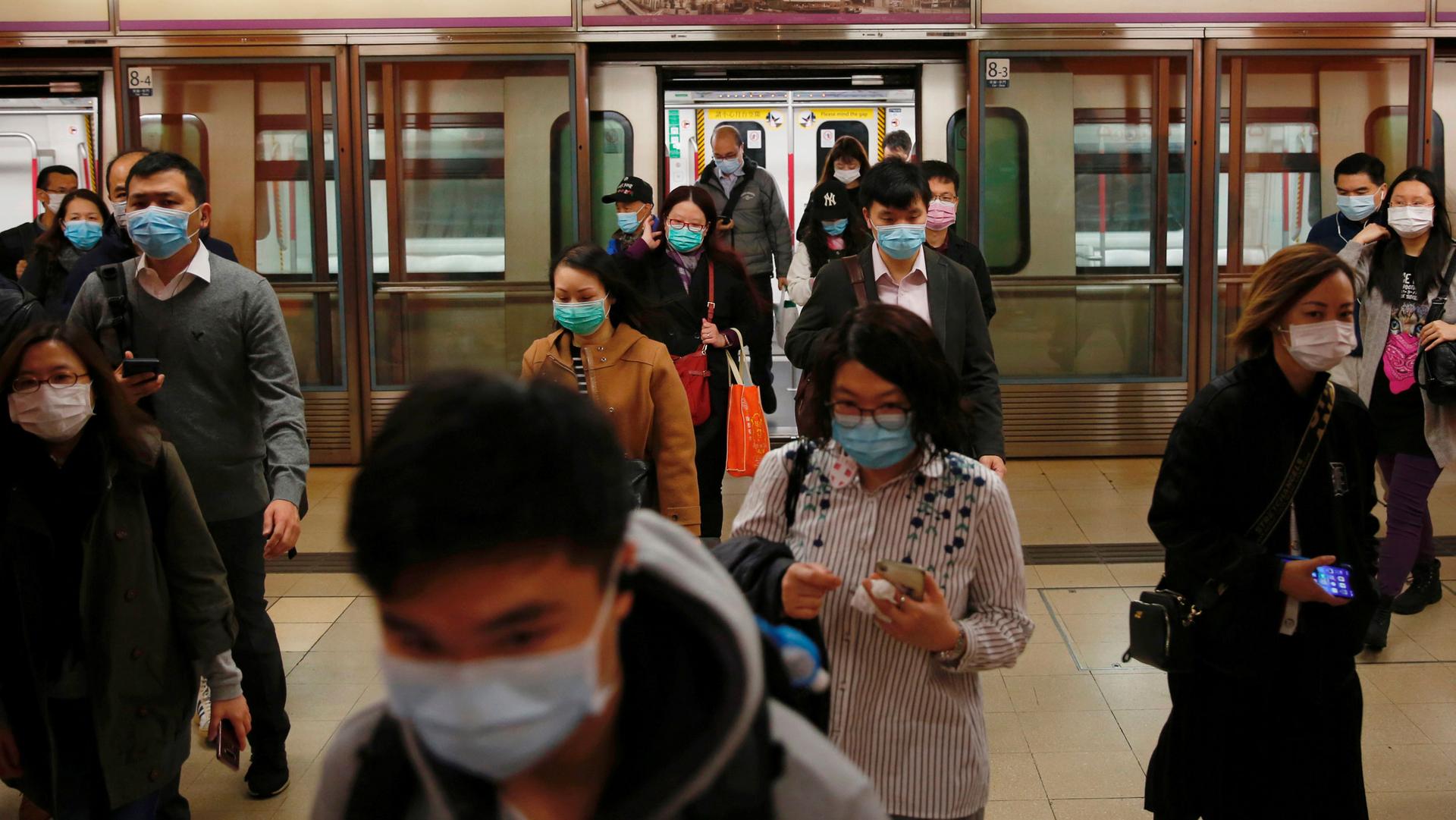 A large group of people are shown exiting a subway train, all wearing blue surgical masks.