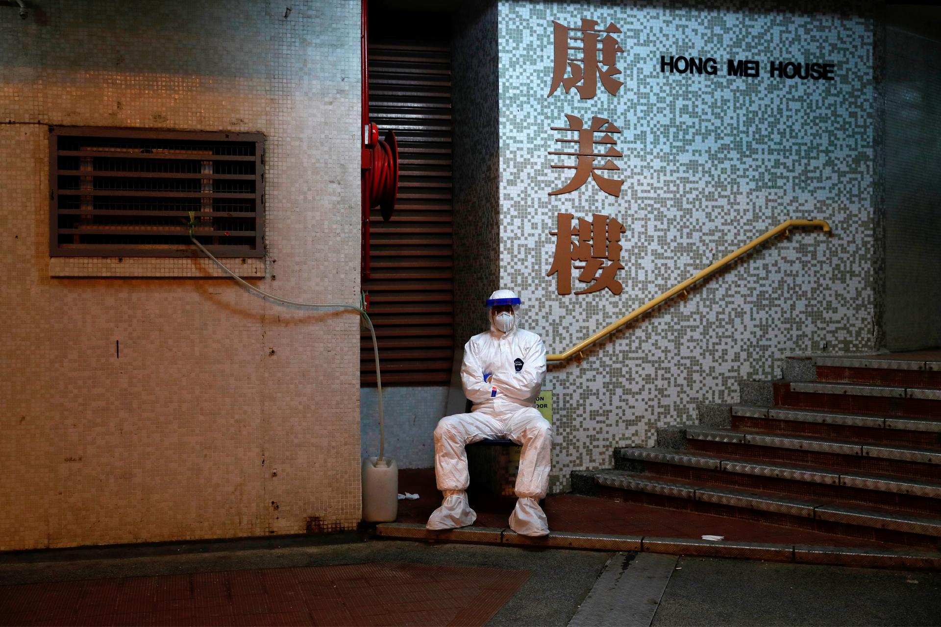 A man in protective gear sits outside a building