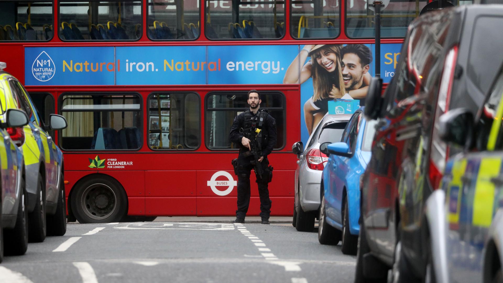 A police officer stands in front of a red London bus