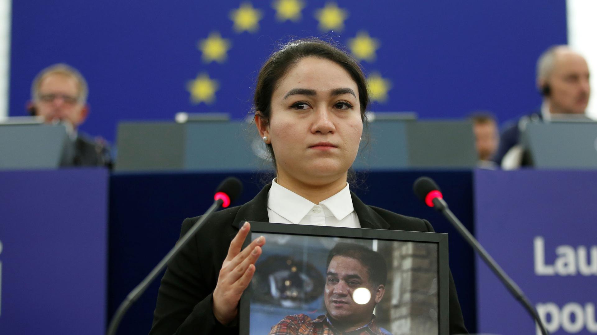A woman stands with a photo of her father