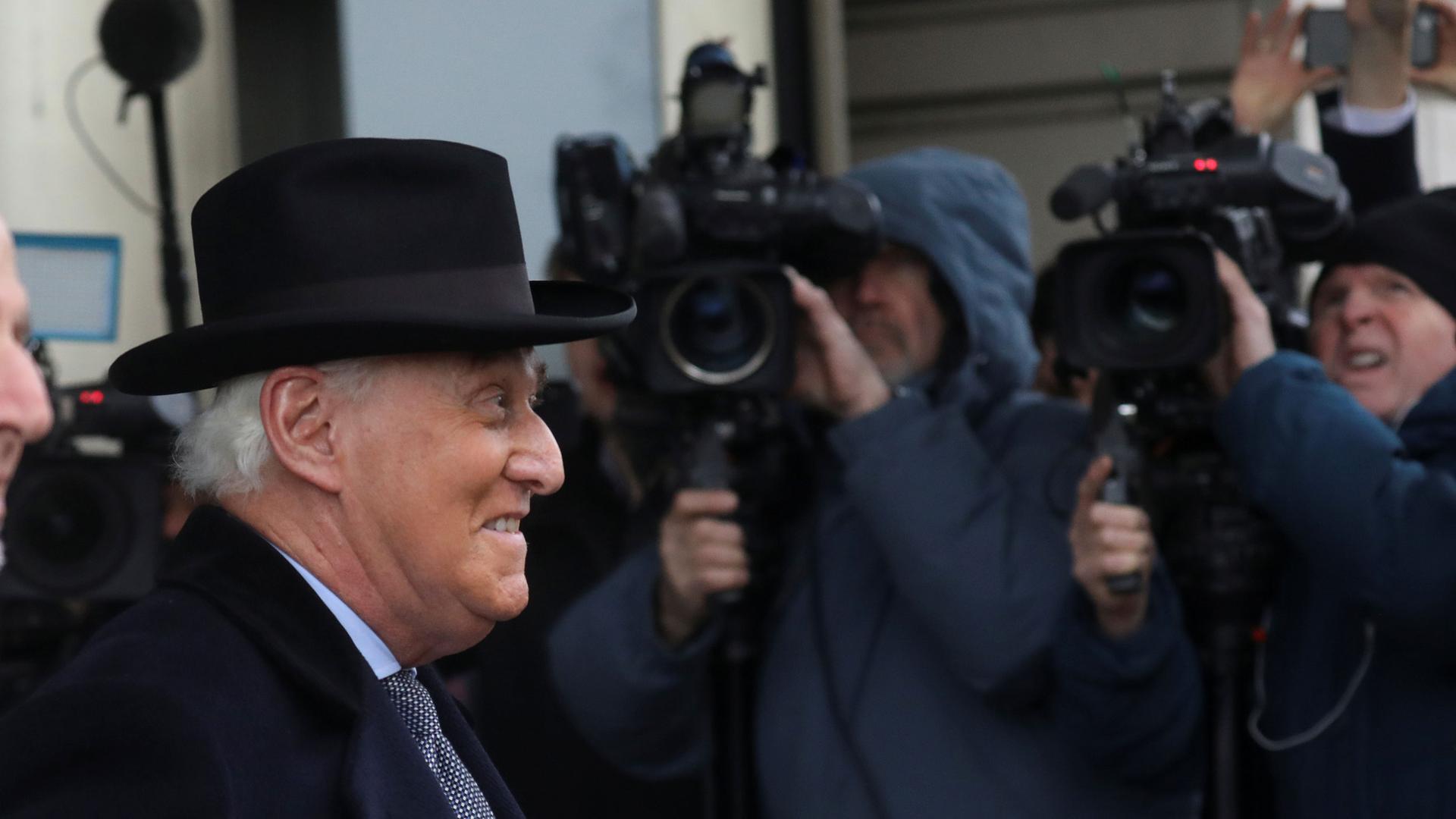 Former Trump campaign adviser Roger Stone is shown wearing a black top hat and overcoat while walking past cameras.