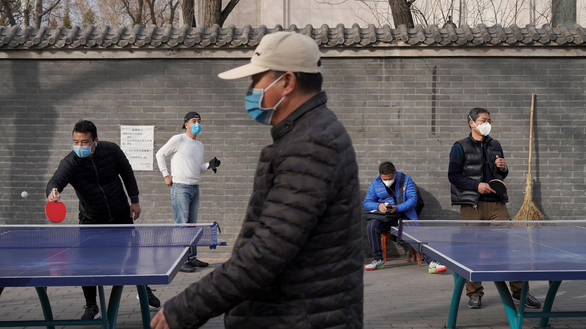 Several people are shown playing table tennis and wearing face masks.