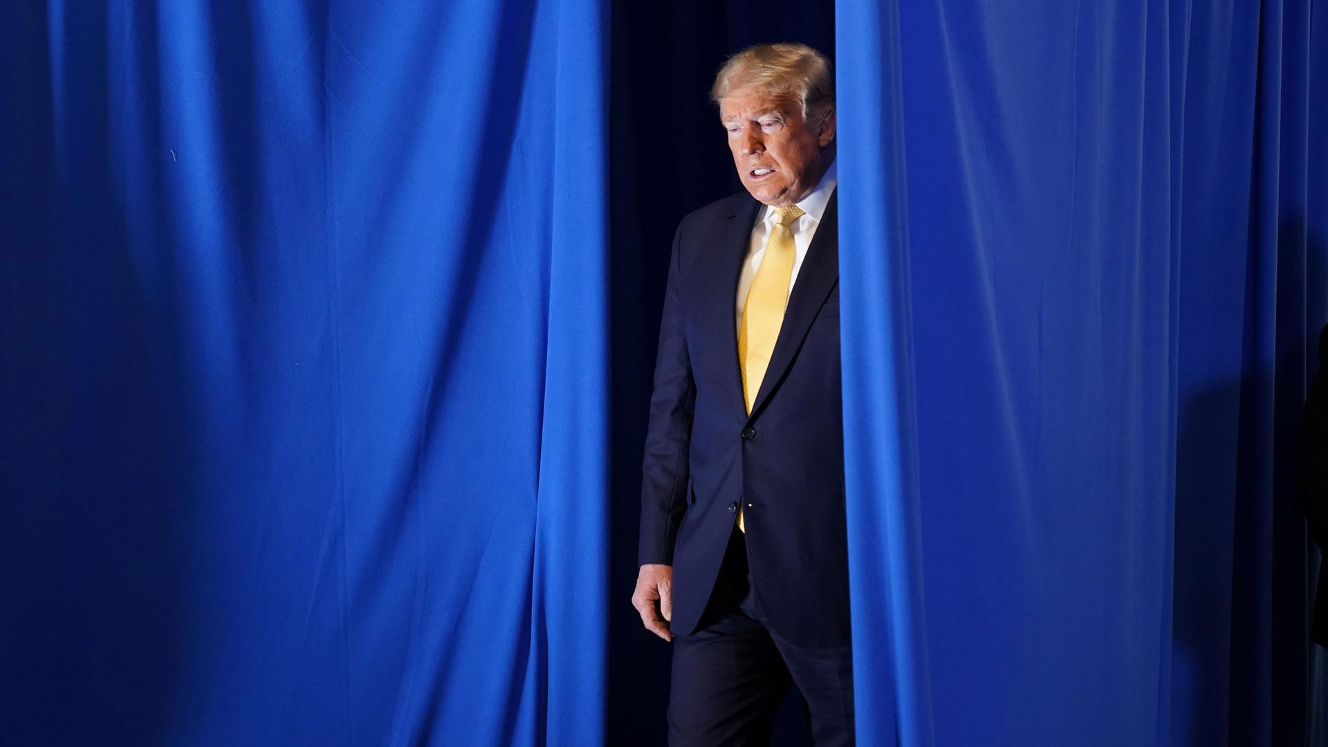 US President Donald Trump is shown walking through a parted blue current and wearing a suit.