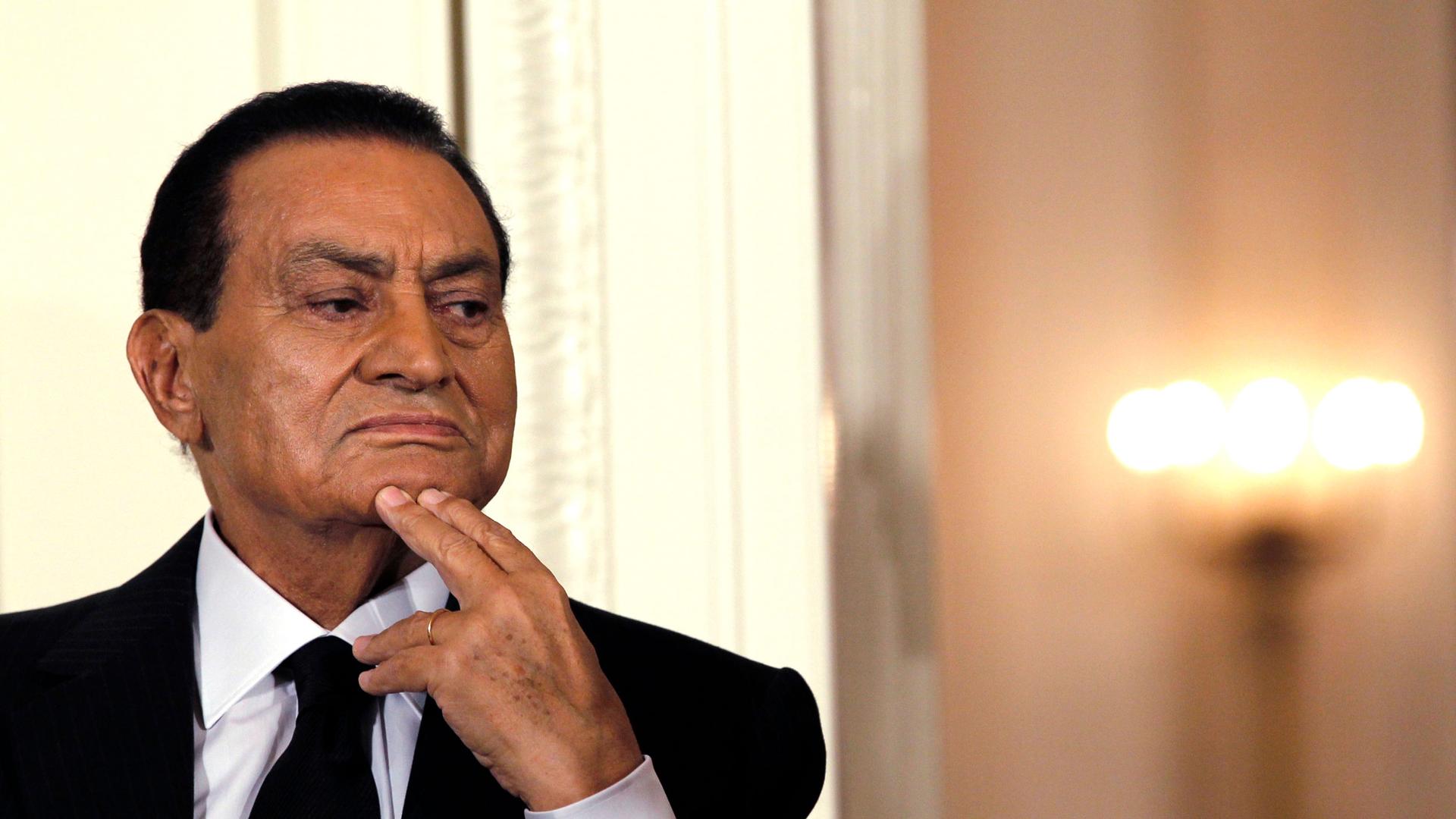 Hosni Mubarak is shown in a close up photograph looking to his left with his chin resting on his hand.
