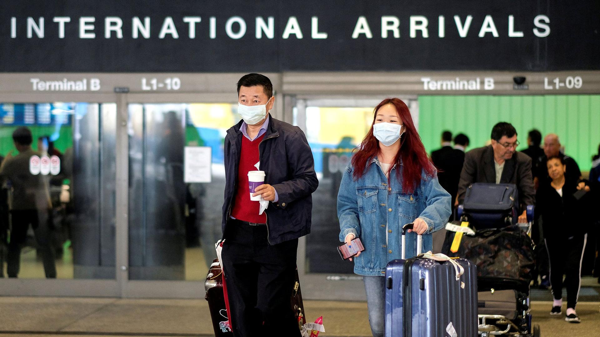 A man and a woman are shown with suitcases and wearing face masks while leaving the international arrivals terminal at Los Angeles International Airport.