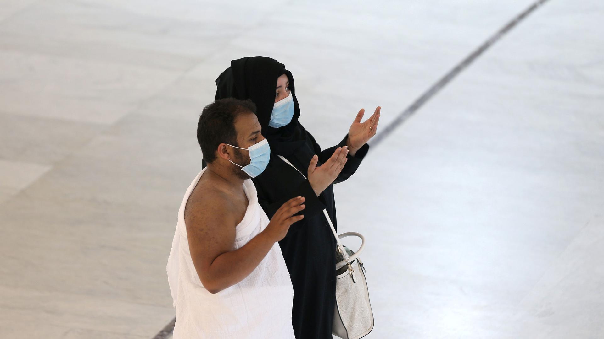 A man and woman are shown standing with their hands in the air and wearing face masks.