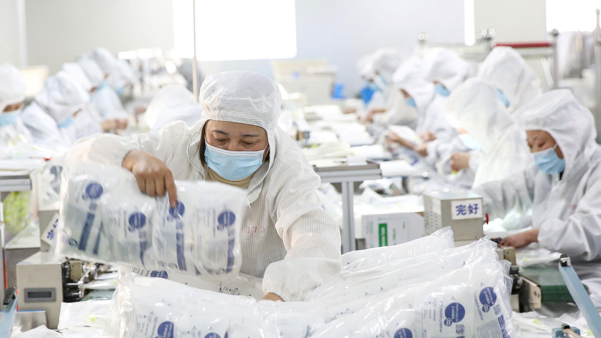 People are shown in all white medical protective gear and face masks while working on a medical supply line.