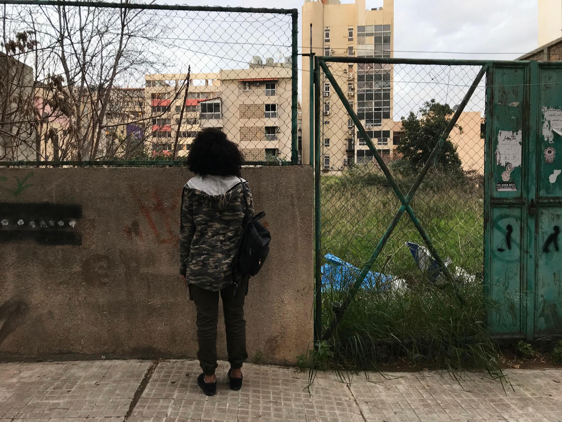 A young woman stands outside looking out at apartment buildings