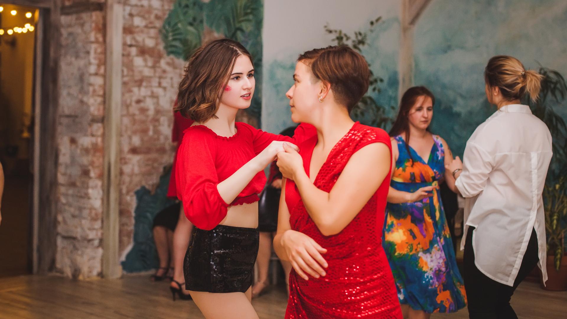 Two women dance together wearing red clothing. 