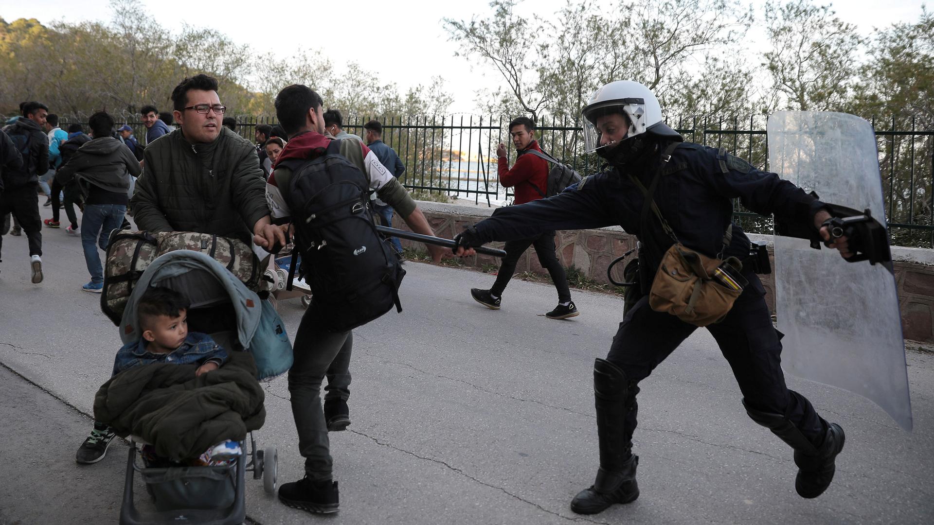 A riot police officer hits a migrant with his baton as police tries to disperse a group of migrants outside the port of Mytilene, Greece, March 3, 2020.