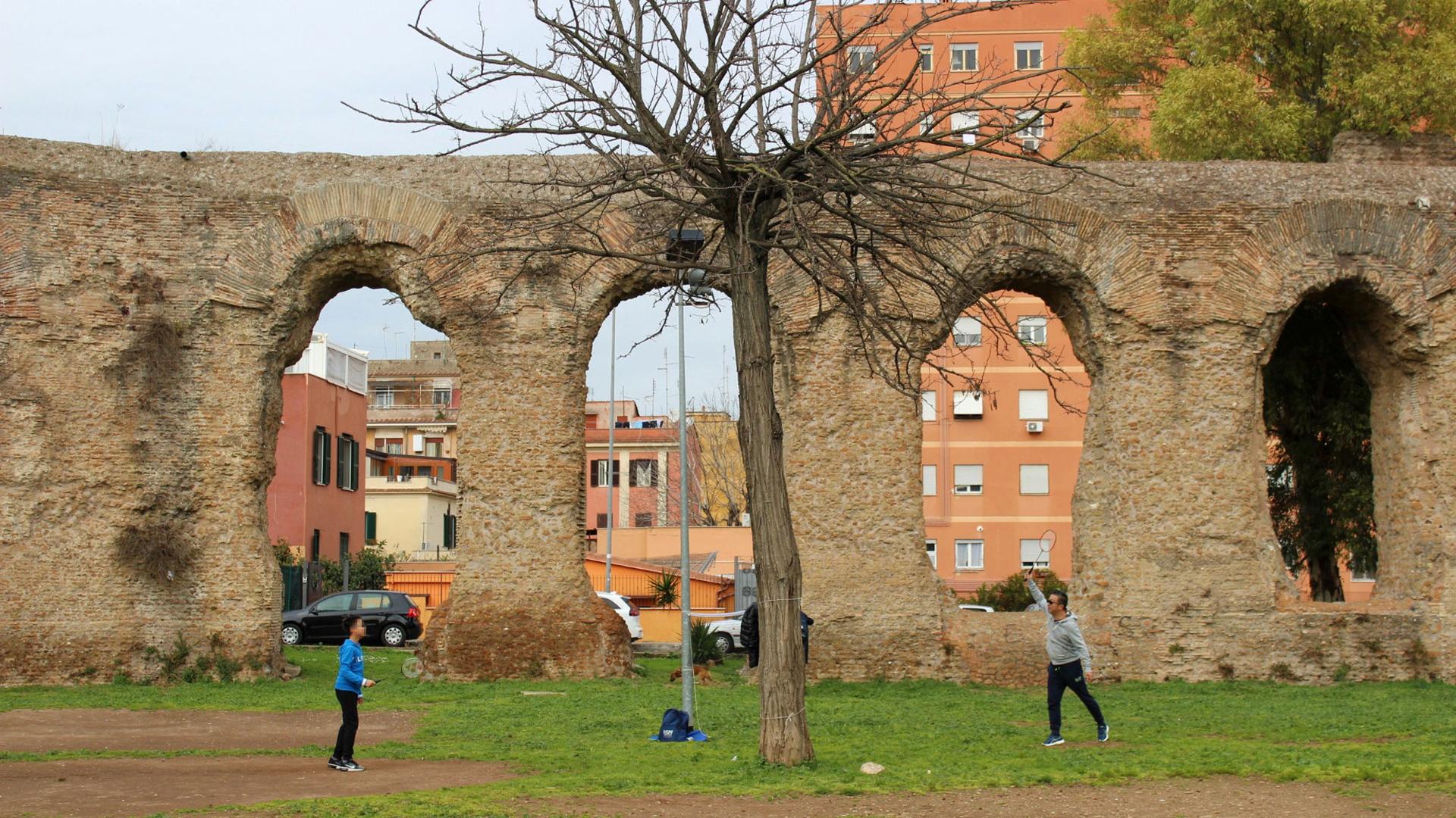 A man and a boy play badminton in front of ruins in a park