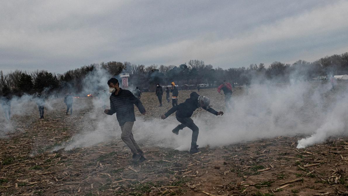 Several men run in a field while teargas is in the air.