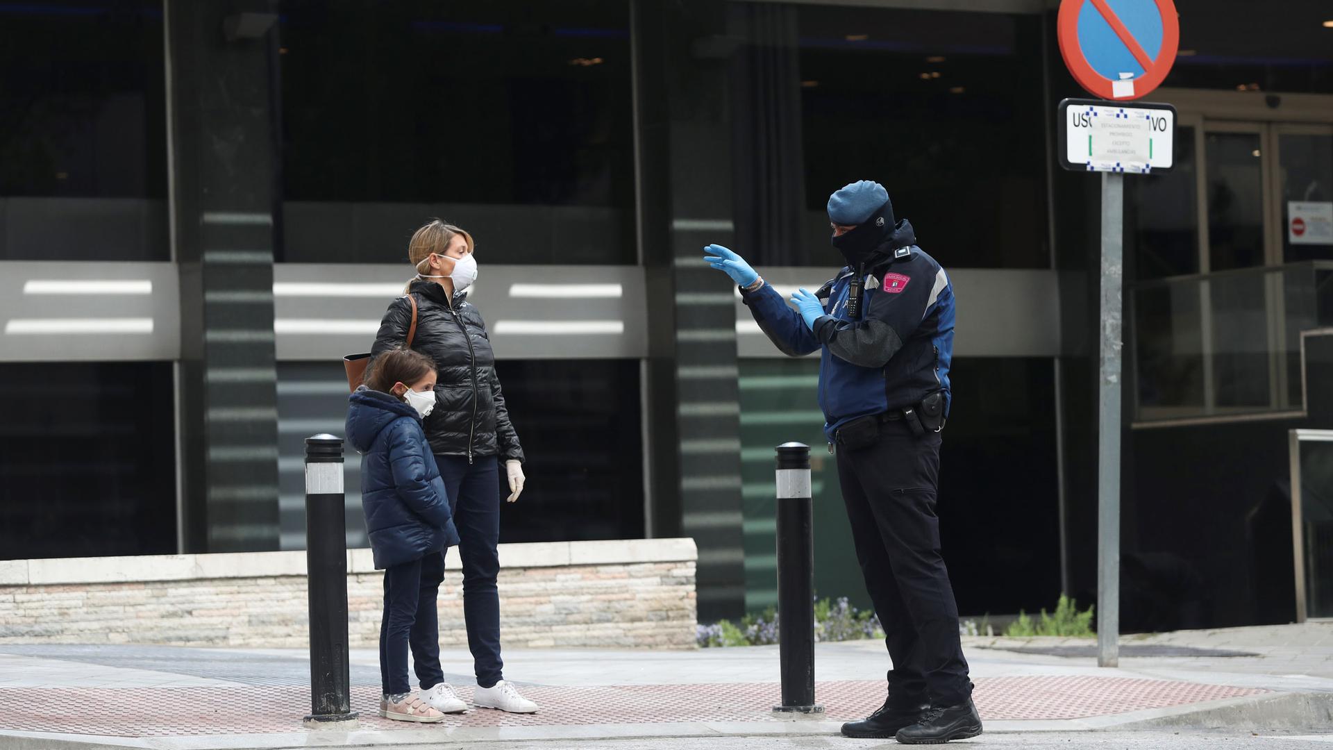 A police officer talks to a woman and child, all in face masks, outside a hotel