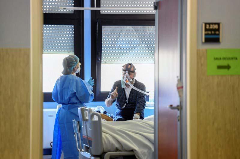 A medical worker wearing a protective mask and suit speaks with a patient suffering from coronavirus disease (COVID-19) in an intensive care unit at the Oglio Po hospital in Cremona, Italy March 19, 2020.