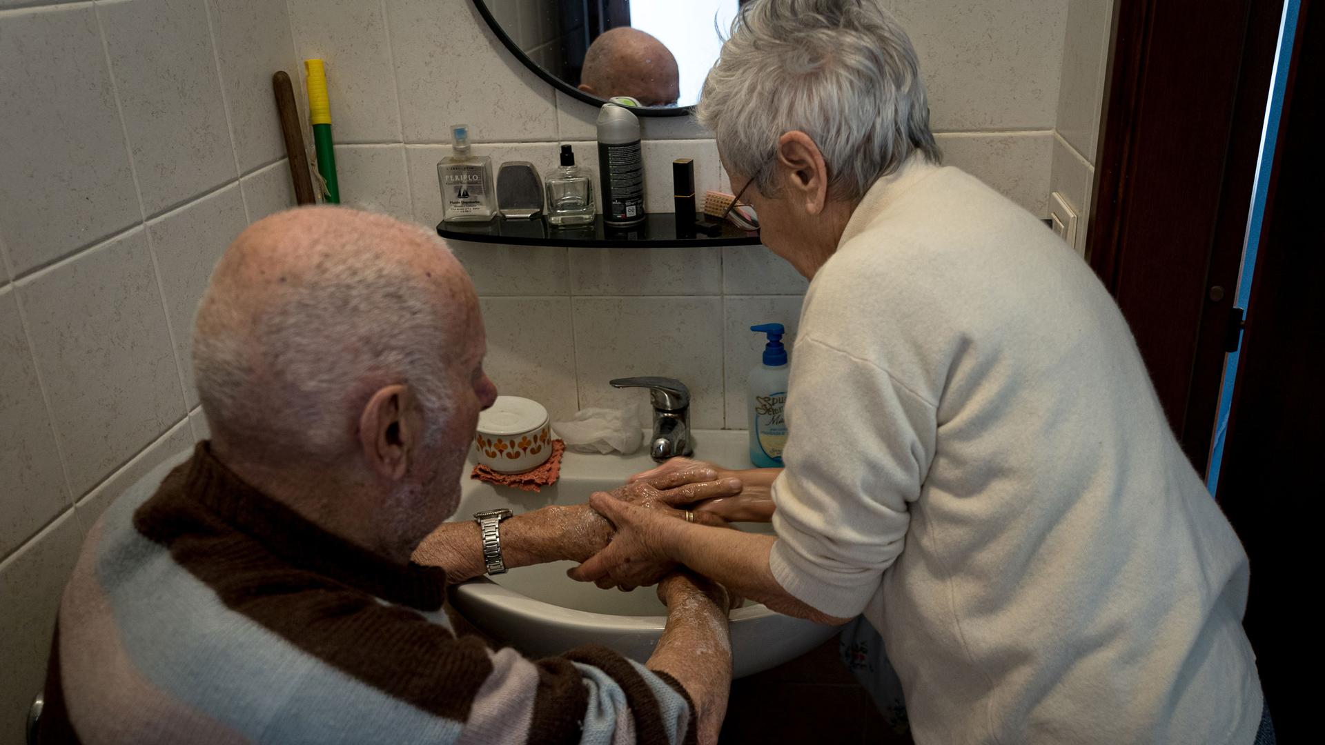 And older woman washes an older man's hands