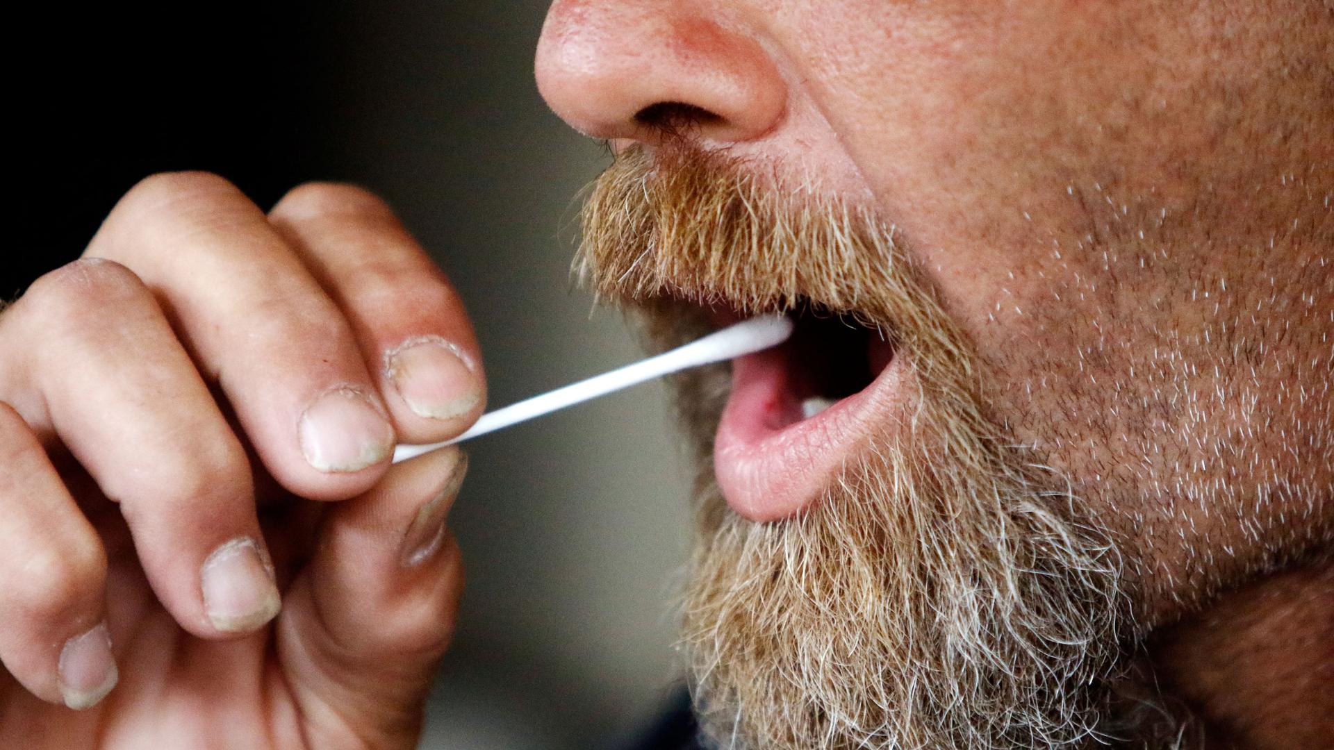 a close up of a man with a beard swabbing his mouth.