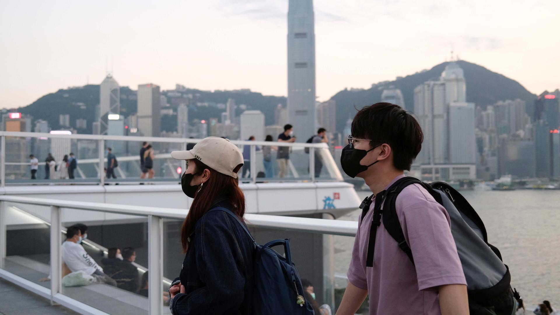 People with protective masks walk in front of Hong Kong's skyline, following the novel coronavirus disease (COVID-19) outbreak, China March 23, 2020.