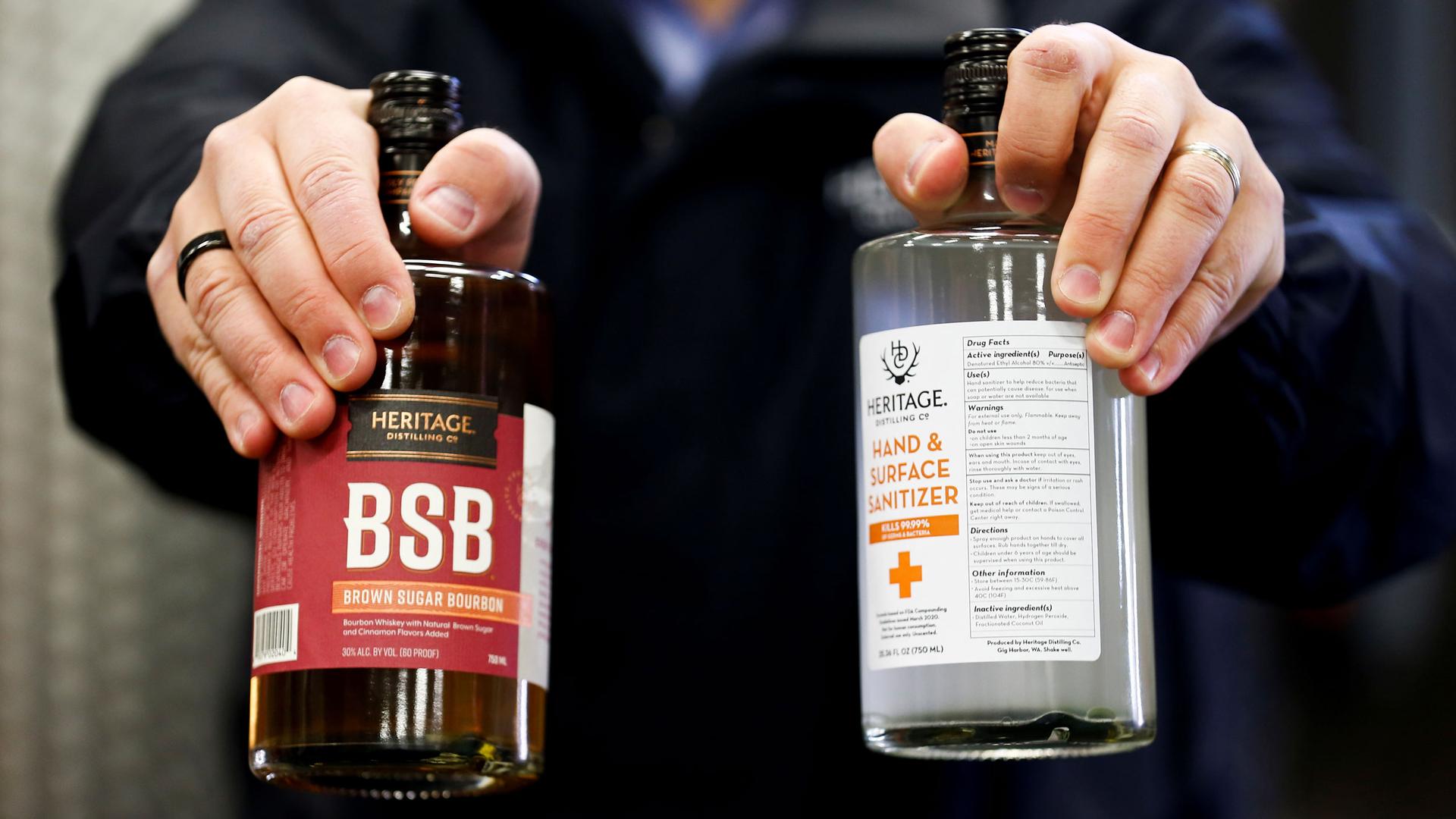 A close up of hands holding a bourbon bottle and a bottle of hand and surface sanitizer