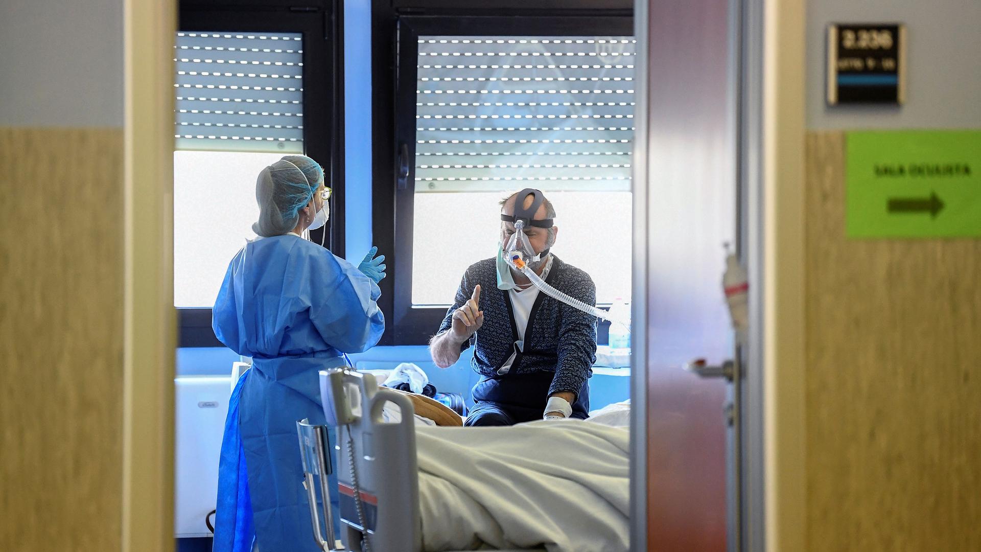 A patient is shown wearing a mask with breathing tubes connected while a medical professional stands adjacent.