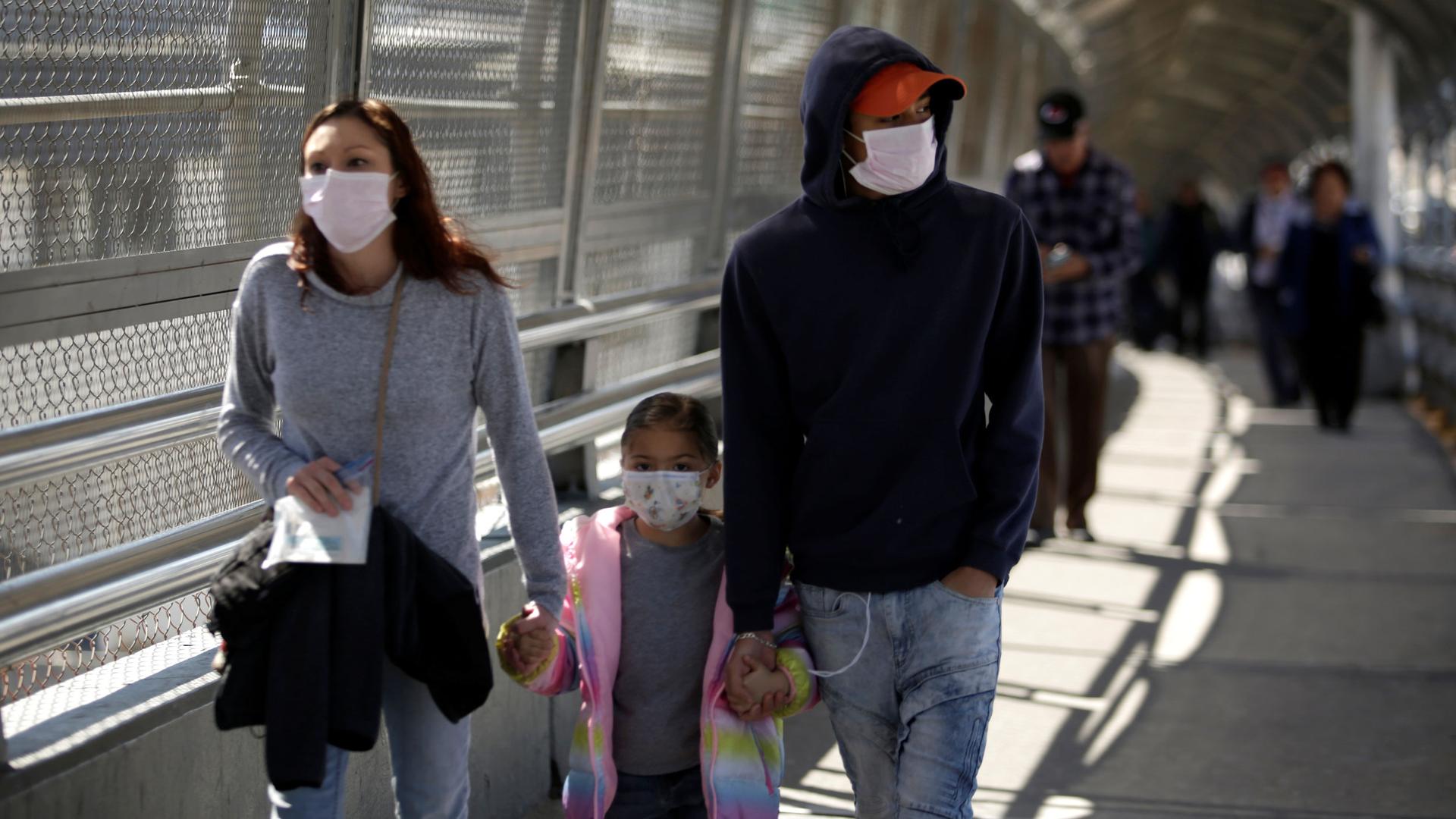 A family wearing protective face masks walks toward the US at the Paso del Norte International Border bridge.