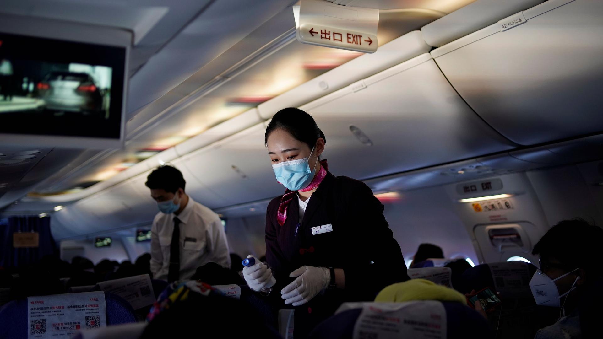 A flight attendant wearing a face mask to prevent the spread of coronavirus disease (COVID-19) takes body temperature measurements of passengers with a thermometer on a Shanghai Airlines flight in Shanghai, China, March 25, 2020. 