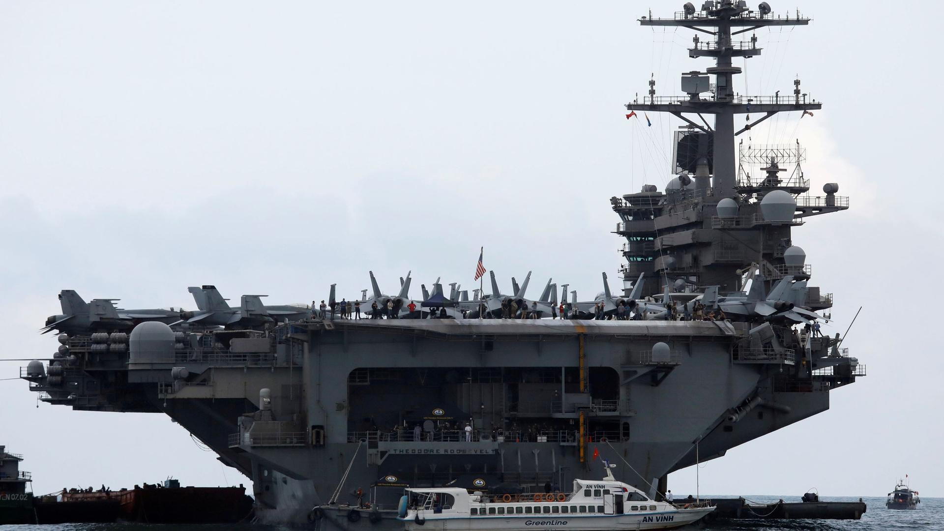 The USS Theodore Roosevelt aircraft carrier is shown from one end with several airplanes parked on the deck.