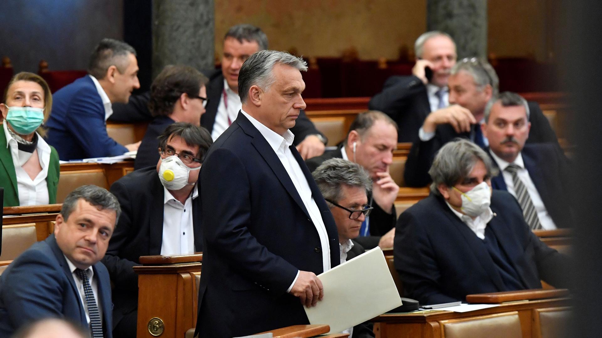 Hungarian Prime Minister Viktor Orban is shown standing among lawmakers and wearing a dark suit jacket.