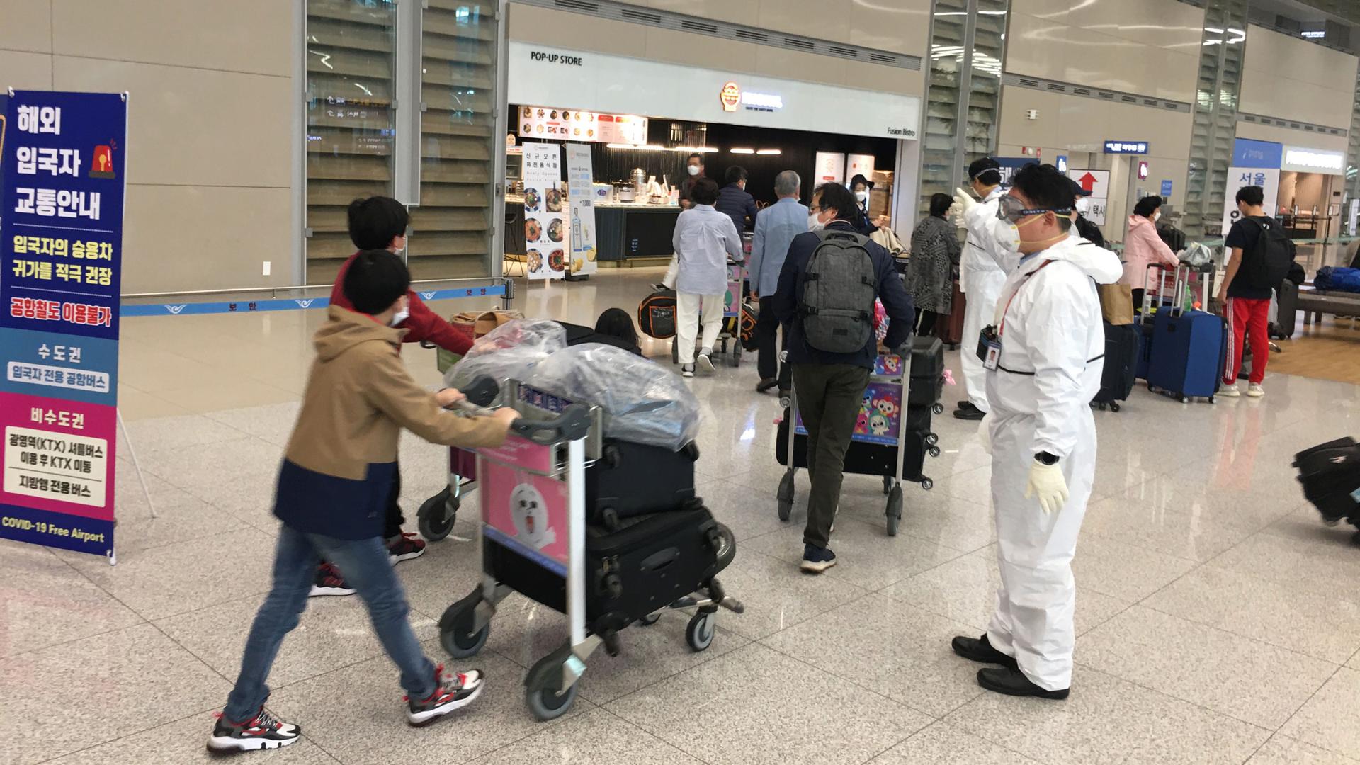 Arrivals at Incheon International Airport are directed by staff in protective gear.